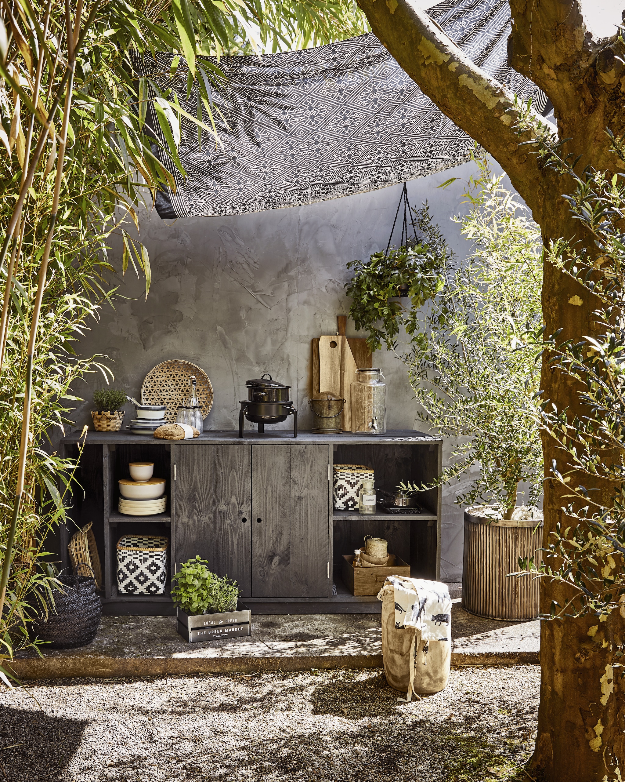 Geribbelde metalen plantenpot, ronde bus met deksel uit India (De Weldaad). Houten kruk, bamboe schalen met houten deksel, grote zwarte emaillen pan, kleine zwarte pannen, ecru borden, zwarte mand, naturel mand in kast set van 4, mandje met plant (Madam Stoltz). Glazen limonadetap, zwart-witte manden, witte emaillen borden, diepe borden, emaillen kommen, flesjes met zwarte dop en rietje (Nordal). Tafelkleed als schaduwdoek, schort, metalen kratje (H&M Home). Laatje van metaal en hout (Burbri Antiek). Gevlochten schaal, houten kommen (HK Living). Barbecue Korpön (Ikea). Overig privébezit.
 vtwonen special 01-2026 | fotografie Jeroen van der Spek | styling Cleo Scheulderman | uitvoering Johan Snoodijk