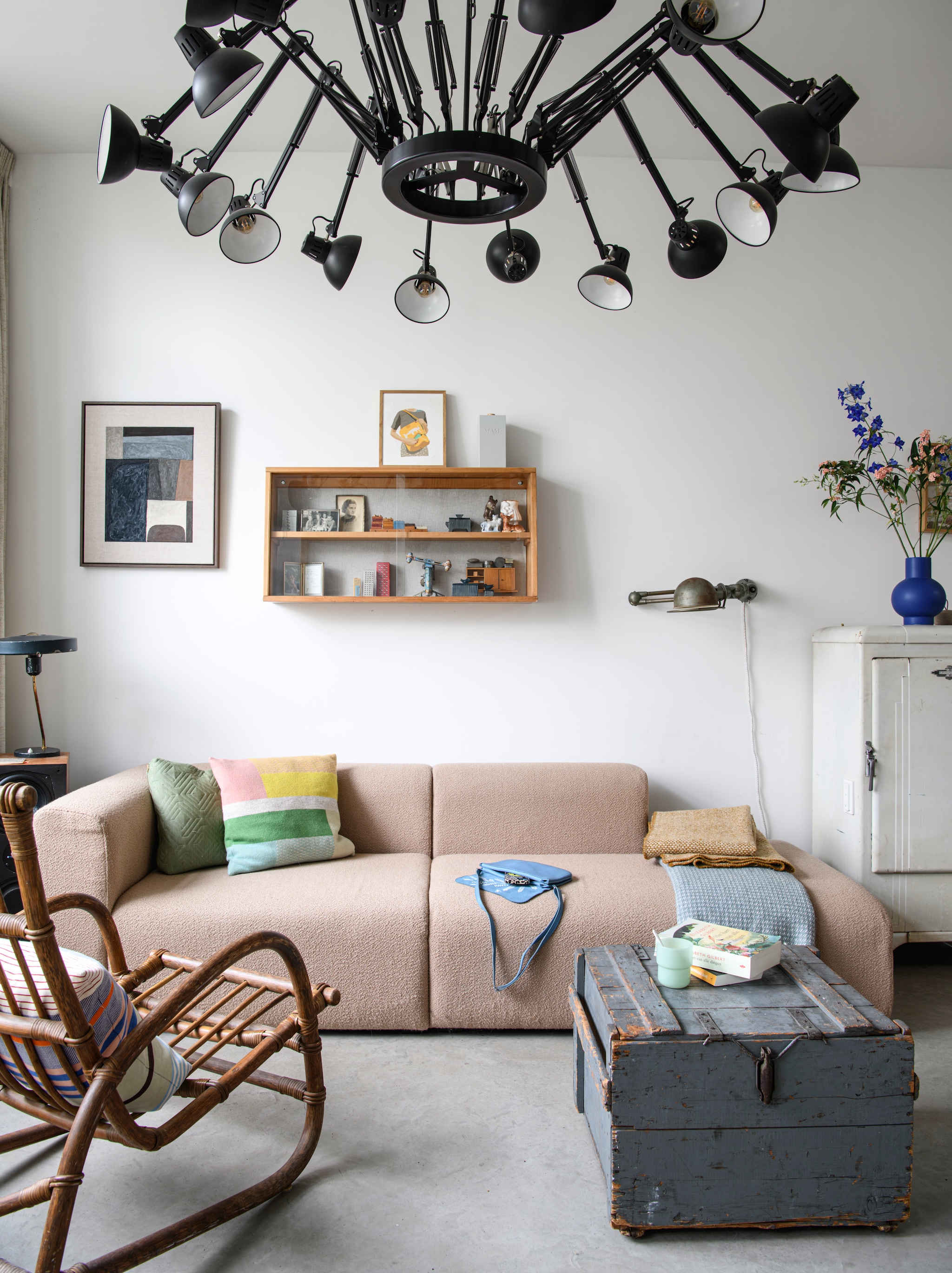 Plafondlamp Dear Ingo van Ron Gilad voor Moooi, tweedehands. Bank Hay. Kussen Manufactum. Oude koelkast omgebouwd tot kast. Bijzettafel oude munitiekist. Wandlamp Jieldé uit Frankrijk. Kunstwerk links Tamasine McNabb. Rotan stoel, vitrinekastje en tafellamp vintage. Klein kunstwerk van Danièle Knirim. Vaas Raawii. vtwonen 04-2026 | styling Kim Timmerman | fotografie Louis Lemaire | productie Insidehomepage