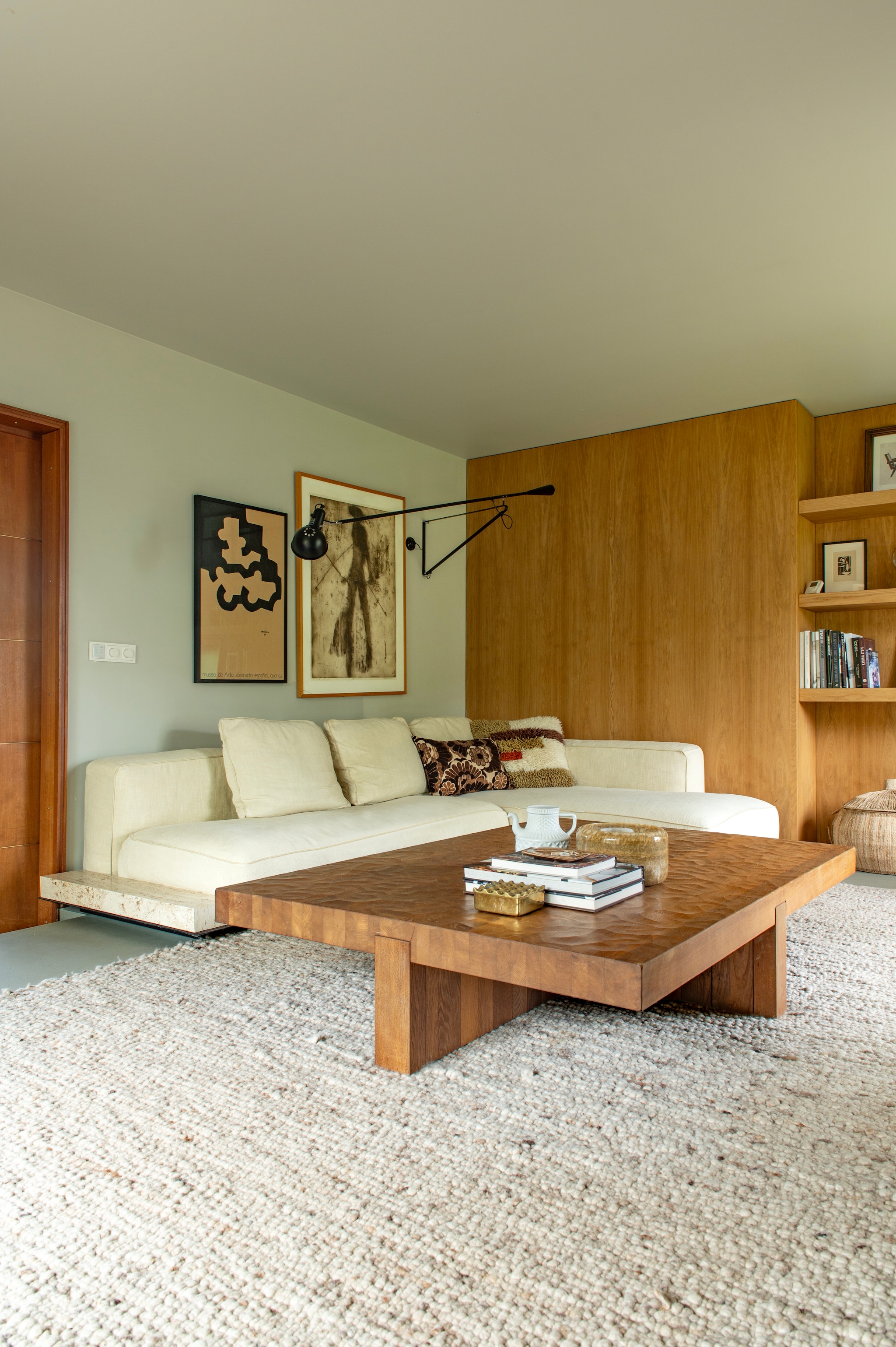 Salontafel van Linteloo via Whoppah. Bank Grandemare van Flexform. Wandlamp 265 van Floss. Kunstwerk rechts Werner Moonen. Kunstwerk links lithografie op kraftpapier Sin Titulo van Eduardo Chillida. Vloerkleed, wollen kussen en windlicht Ony via Bynord. Bloemkussen HKliving. Theepot Sargadelos. Kleur wand en plafond Old Flax van Pure & Original. vtwonen 04-2026 | styling Jeske Weel | fotografie Caroline Coehorst