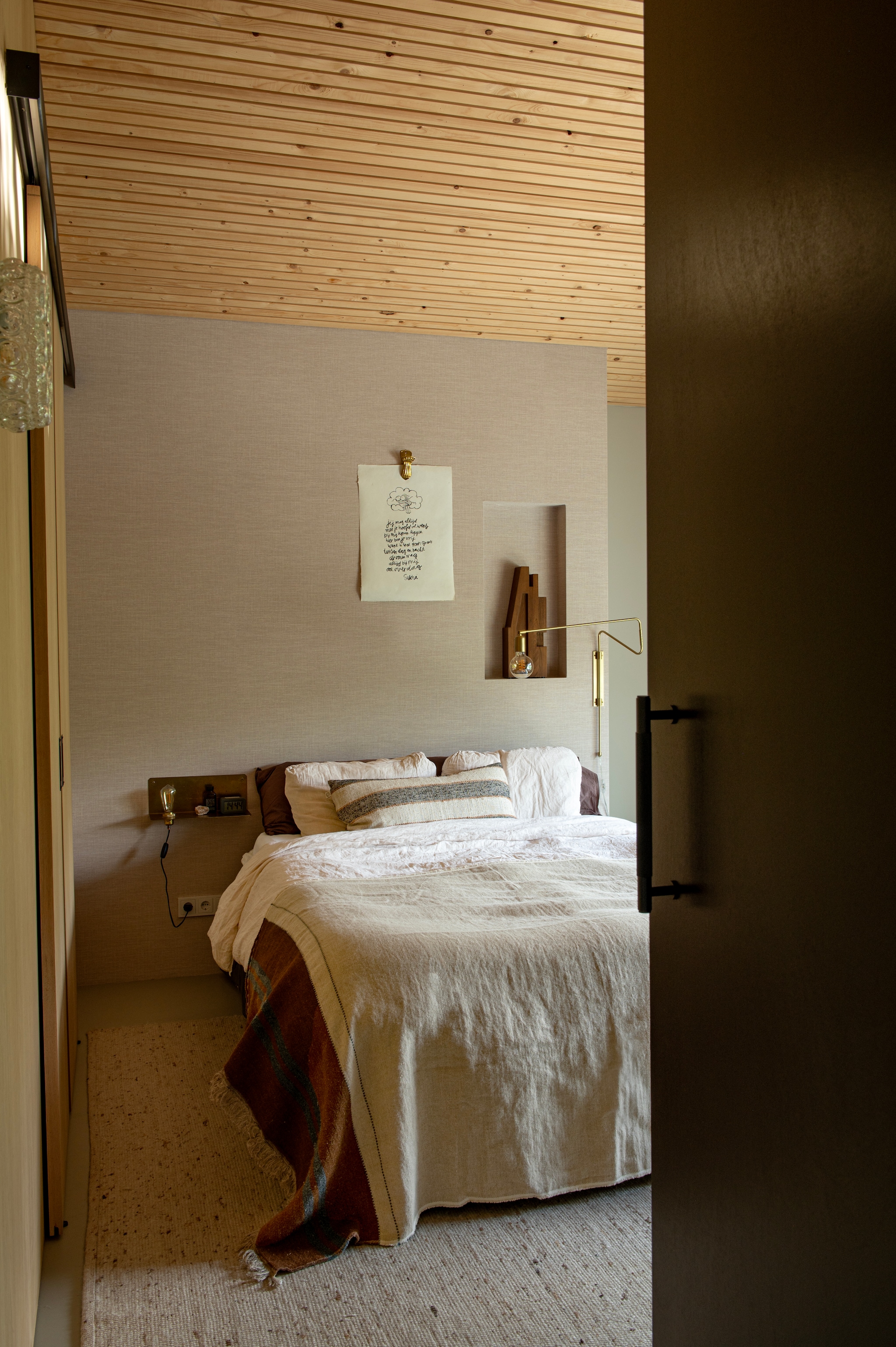 Wandlamp House Doctor. Nachtkastje Frama. Poster Sukha. Sprei Libeco. Kussen en sculptuur Bynord. Behang Le Rideau. Muurverf Coffee Cream van Pure & Original. vtwonen 04-2026 | styling Jeske Weel | fotografie Caroline Coehorst