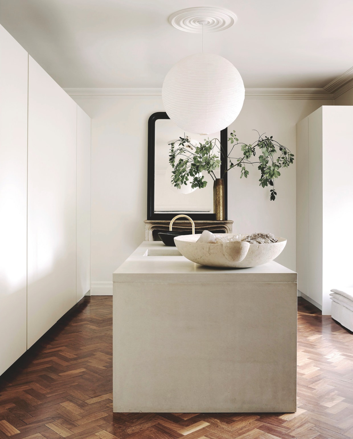 Kookeiland van gegoten beton. Keukenkasten op maat gemaakt door een timmerman. Achter de kamerhoge deuren is alle apparatuur en serviesgoed verborgen. Kraan Vola. Oude schouw en spiegel uit Frankrijk. Bollamp Hay. Koperen vaas is een vintage patroonhuls. vtwonen Landelijk 01-2026 | styling Ali Heath | fotografie Michael Sinclair