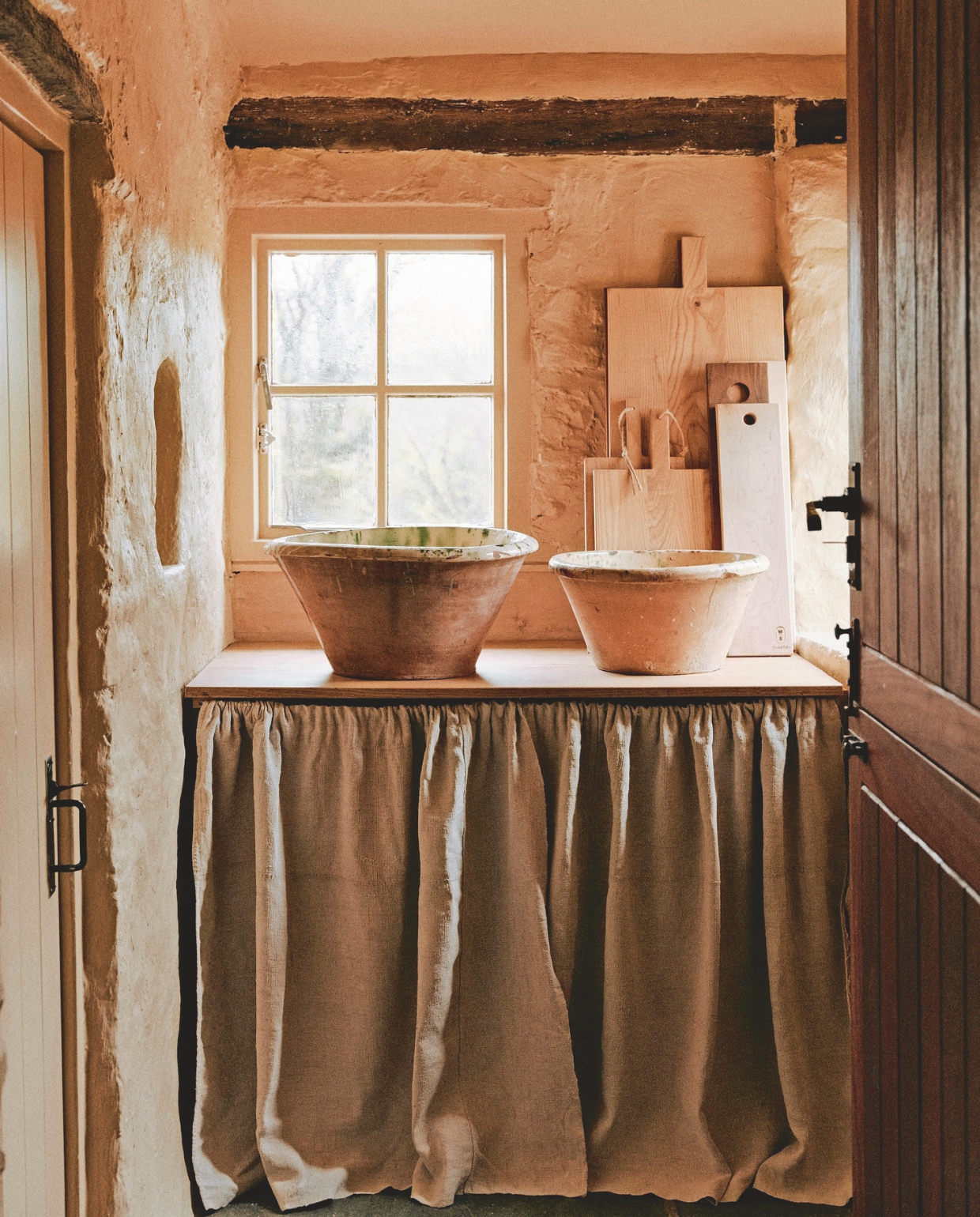 Een linnen gordijn onttrekt de opbergruimte aan het zicht, waardoor deze hoek zijn rustieke eenvoud behoudt. vtwonen Landelijk 01-2026 | styling Ali Heath | fotografie Michael Sinclair