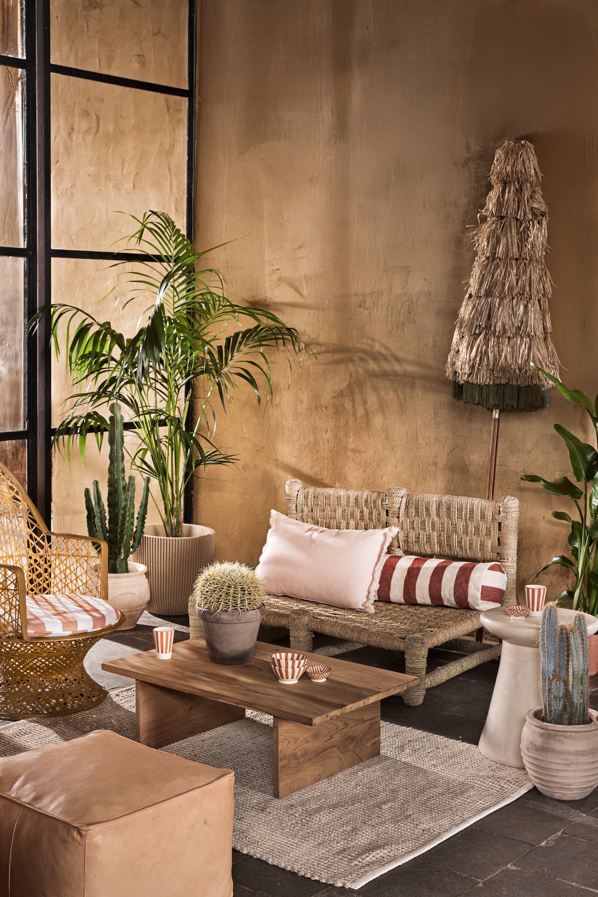 Household Hardware loungebank Hassan, hout en touw € 515,-, bijzettafel Champignon, tadelakt € 359,-, fauteuil Vanessa, gevlochten draad, bruin € 485,-, rolkussen, wol, terra/wit, 100 cm (l) € 189,-, kom Fez, keramiek, terra/wit, per stuk € 8,25, mokken Fez, keramiek, terra/wit € 12,50, schaaltjes Fez, keramiek, terra/wit € 12,50 (householdhardware.nl). Raw Materials salontafel Thar, teakhout € 419,- (rawmaterials.eu). Intratuin vloerkleed Miyanna, jute en katoen, naturel, 180x120 cm (lxb) € 54,99, pot, terracotta met bogen € 69,99, pot, terracota met strepen, blond beige € 99,99, Mica Outdoor pot Stan, terracotta, grijs € 5,79, Capi Europe pot Groove met ribbels € 49,99 (intratuin.nl). HKliving parasol Serengeti, polyester en hout, 230 cm (Ø) € 439,- (hkliving.nl). vtwonen special 01-2026 | styling Marlies Does | fotografie Peggy Janssen