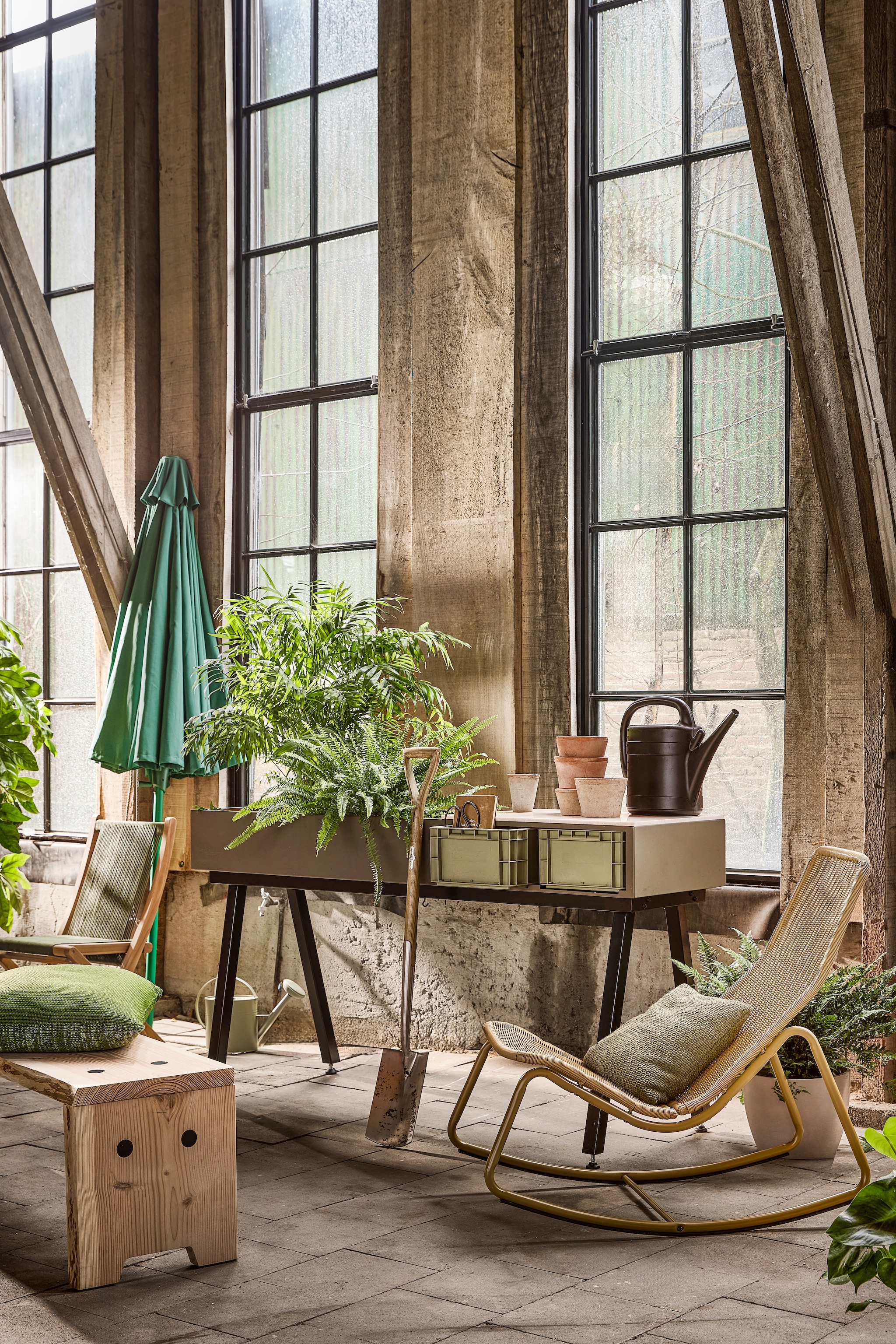 Woood schommelstoel Tom, kunststof en metaal, honinggeel € 159,- (woood.nl). Weltevree bank Forestry, Douglashout, vanaf € 750,-, werkbank Gardenworks Station, solid surface, staal en aluminium, groen € 1350,- (weltevree.eu). Raw Materials klapstoel Rope, hout en gevlochten zitting, groen € 199,- (rawmaterials.eu).  Zwarte gieter € 7,99, groene gieter € 19,99, terracotta potten vanaf € 4,99, spade € 69,99, (intratuin.nl). Paola Lenti kussen, gebreid, groen€ 641,- (dacks.nl). Zuiver parasol Sunshine, polyester, exclusief voet € 109,- (zuiver.com). vtwonen special 01-2026 | styling Marlies Does | fotografie Peggy Janssen