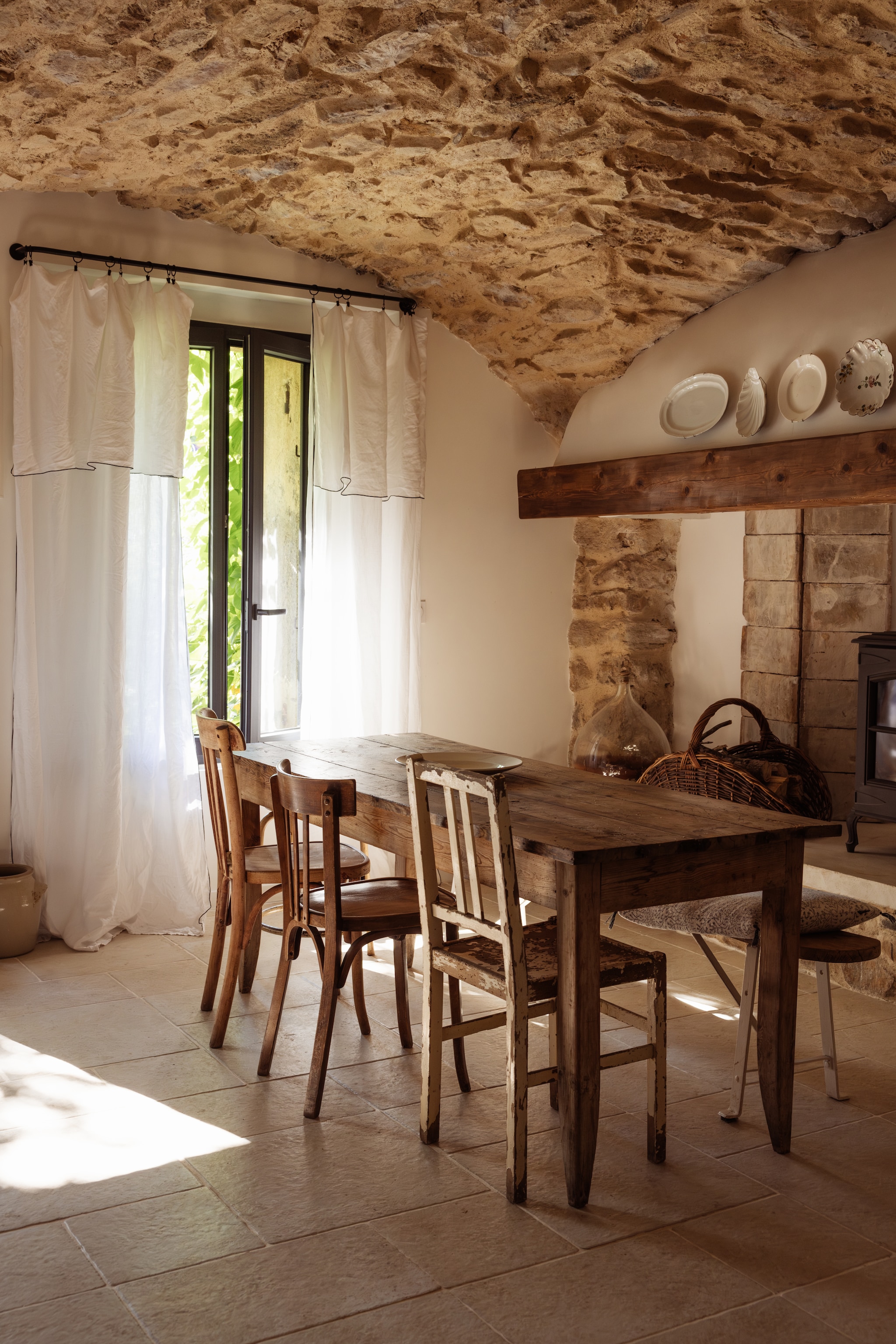 Linnen gordijnen Cyrillus. Tafel, stoelen en borden brocante. Gietijzeren houtkachel Invicta. vtwonen Landelijk 04-2026 | Fotografie Dana van Leeuwen | Styling Ilona Jongepier