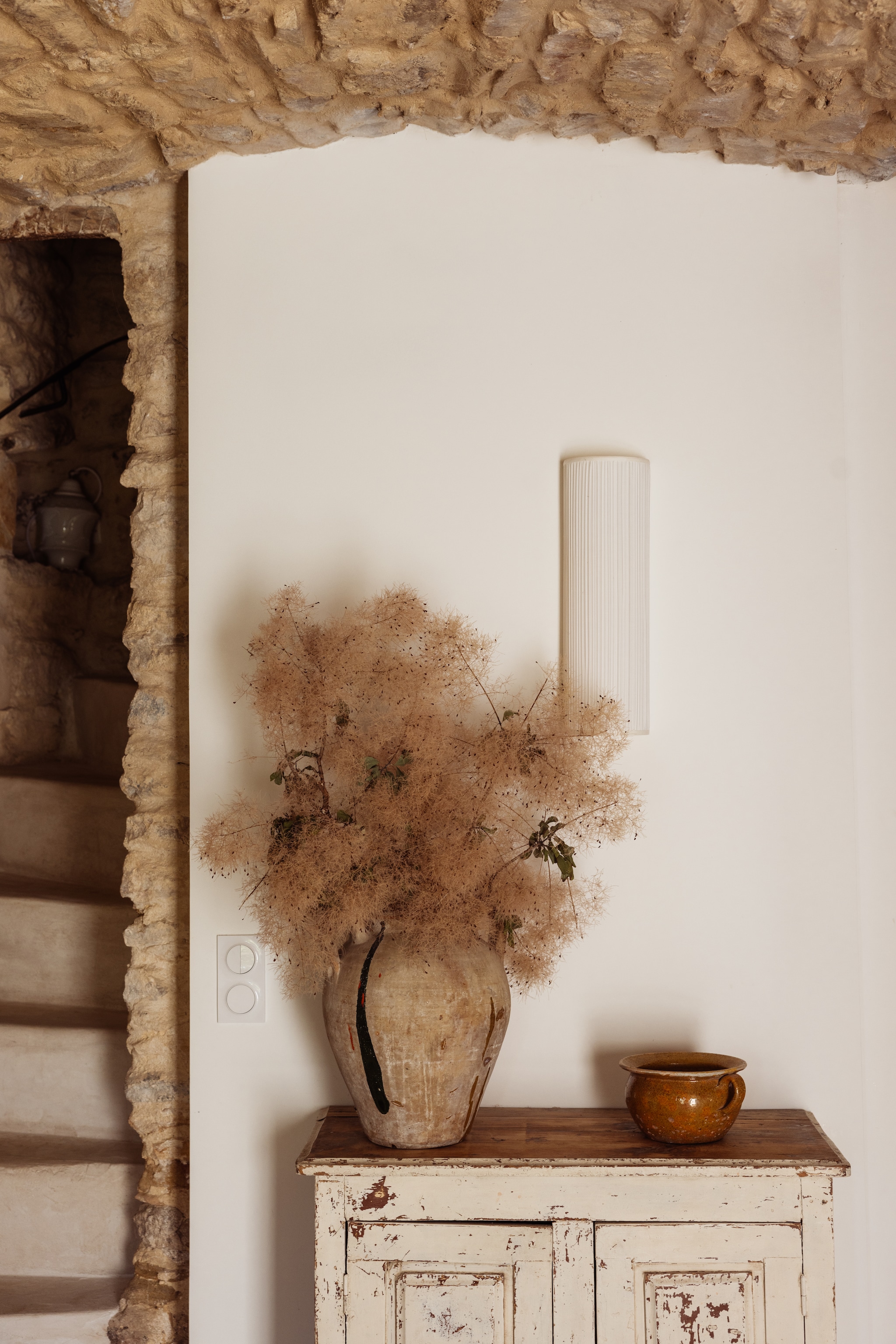 Houten kast Atelier Marchal. Wandlamp The Socialite Family. Vaas en pot brocante. Gedroogde pruikenboomtakken uit de tuin. vtwonen Landelijk 04-2026 | Fotografie Dana van Leeuwen | Styling Ilona Jongepier