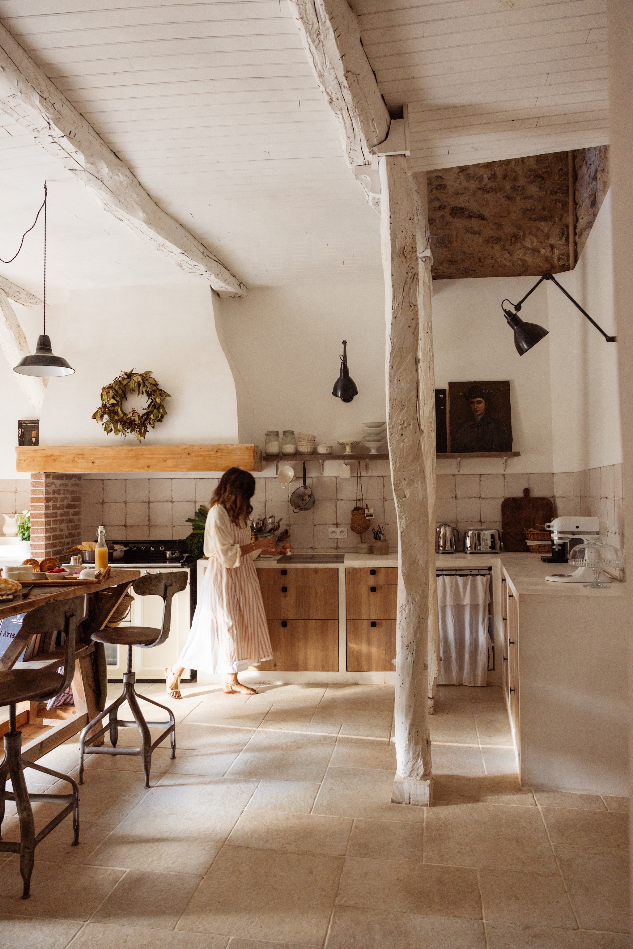 Het kookeiland gemaakt van een oude werkbank. Waterkoker, broodrooster, keukenmachine Smeg. Atelierstoelen, schilderijen, schalen, potten, broodplank en lampen brocante. Linnen gordijn zelfgemaakt. vtwonen Landelijk 04-2026 | fotografie Dana van Leeuwen | styling Ilona Jongepier