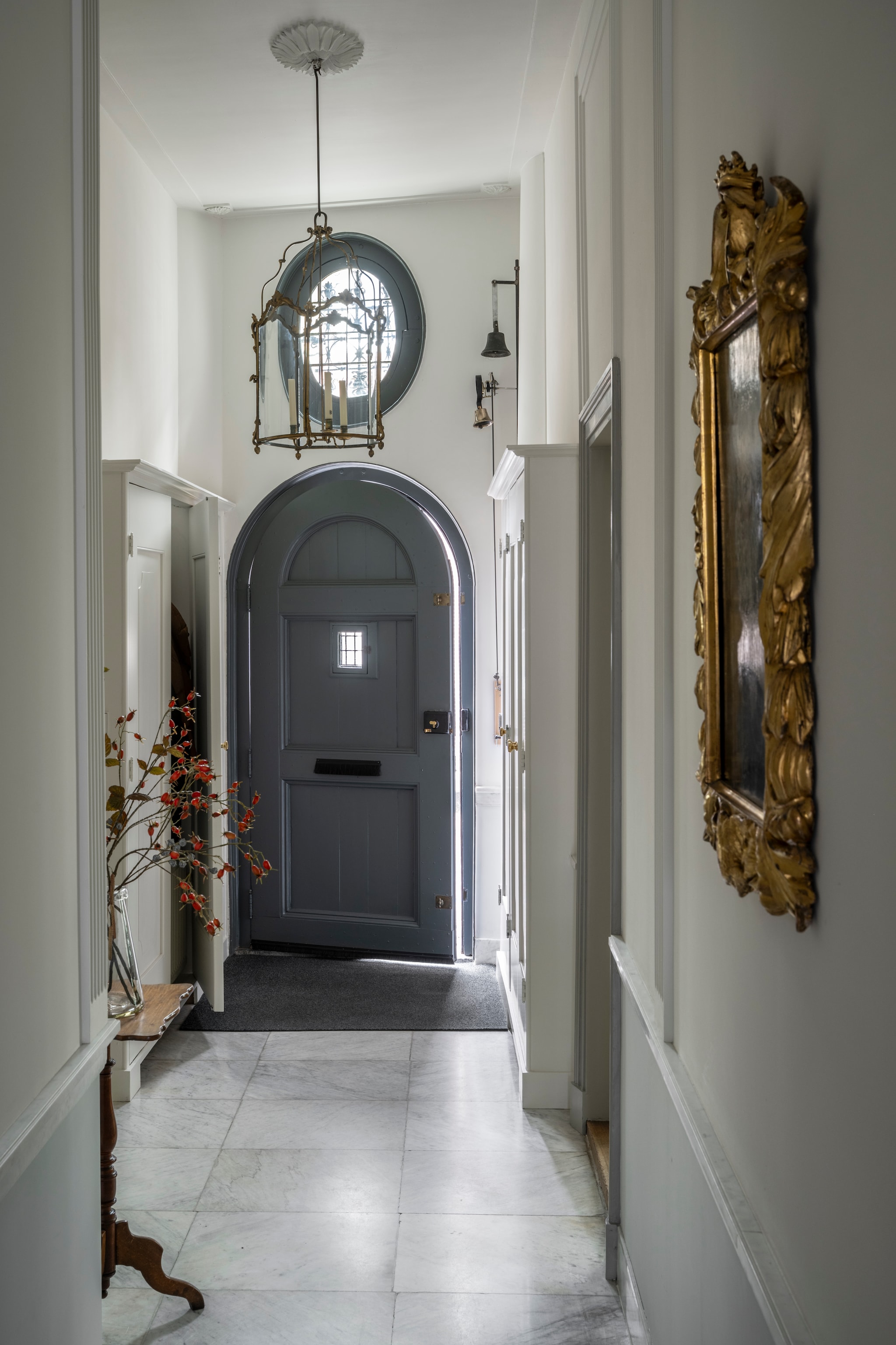 De gedeelde voordeur met twee deurbellen en aan weerszijden kasten voor de jassen. Tafel erfstuk. Lamp gekocht op een veiling. Tegels zaten al in het huis.  vtwonen Landelijk 04-2026 | styling Marianne Luning | fotografie Stan Koolen