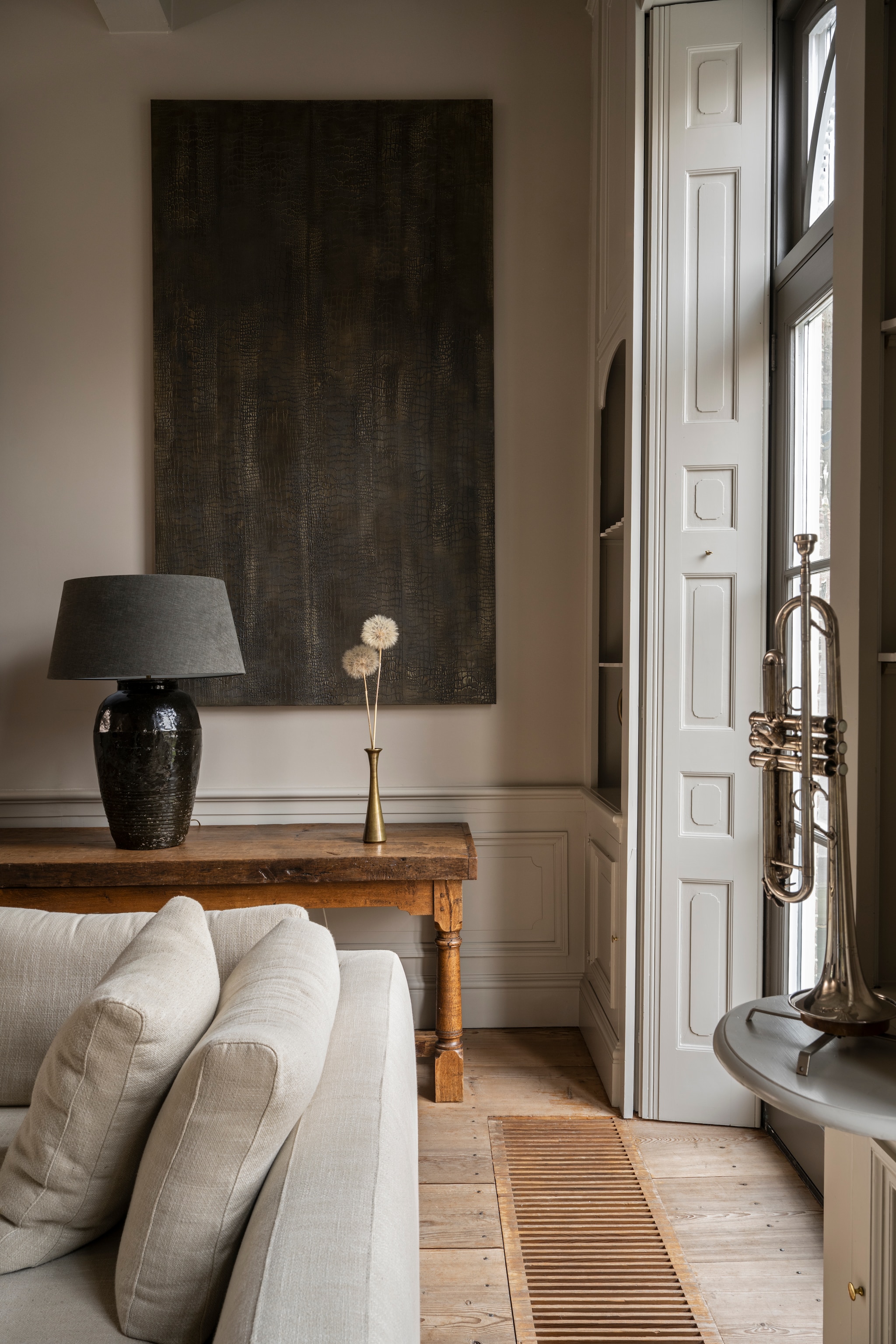 Panelen aan de muur Jb Interior Design. Sidetable gemaakt door vader van Cor. Kruiklamp met kap Het Kabinet. Bronzen vaas rommelmarkt. Bank Eijerkamp. Trompet Antoine Courtois. Luiken zaten al in het huis. vtwonen Landelijk 04-2026 | styling Marianne Luning | fotografie Stan Koolen