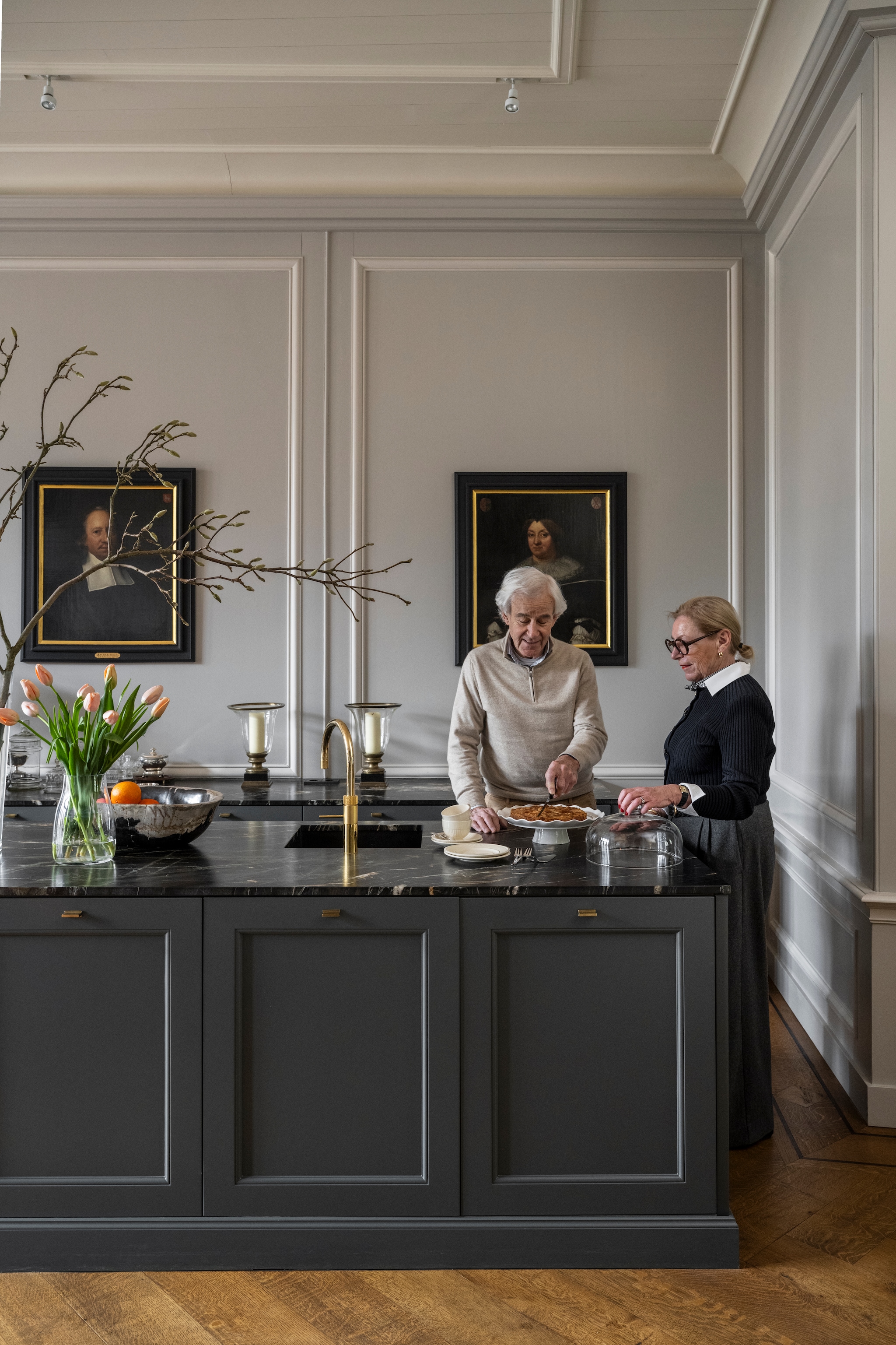 Muurkleur Purbeck Stone, Ammonite en achtergrond boekenkast Mole’s Breath van Farrow & Ball. Keuken, wandbetimmeringen en parketvloer Aannemersbedrijf Leguit en Roos. Kraan Quooker. Vaas Bloemisterij Roos Monnickendam. Schaal Ambiance Laren. Schilderijen en windlichten veiling. Taartplateau cadeau. vtwonen Landelijk 04-2026 | styling Marianne Luning | fotografie Stan Koolen