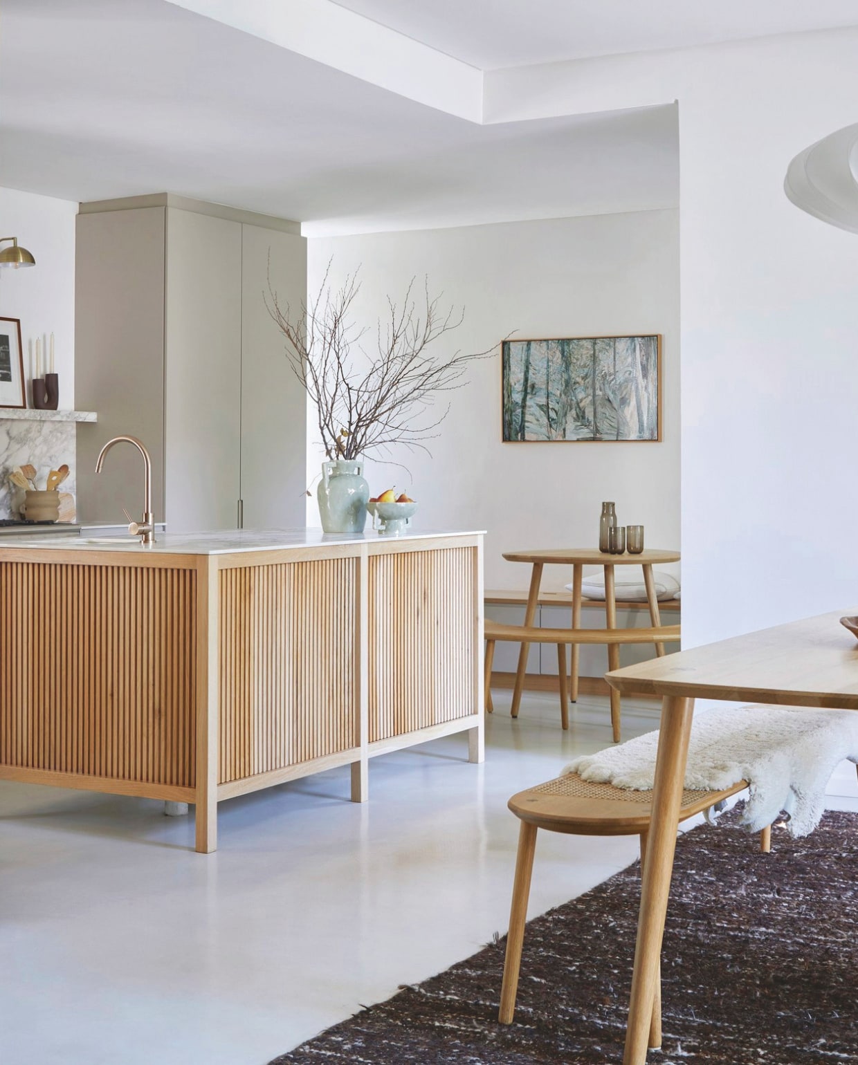 Keukeneiland bekleed met eikenhout. Fruitschaal en vaas @home. Beide tafels met banken Houtlander. Karaf en glazen H&m Home. vtwonen 02-2026 | styling Sven Alberding | fotografie Greg Cox