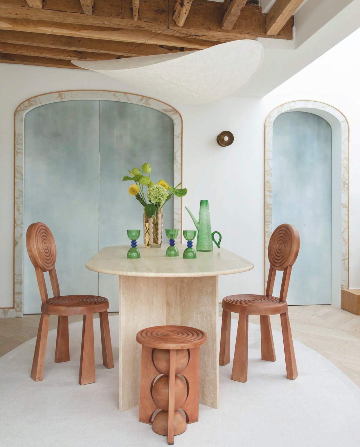 Travertin tafel Talka. Stoelen, kruk, vaas Batiik Studio x Monoprix. Karaf Maximilien Pellet x Monoprix. Glazen Caroline de Benoist x Monoprix. Hanglamp Tense van New Works. Schuifdeuren beschilderd door Fanny Chaix Bryan. Tegels rondom deur Calacatta di Oro. Vloerkleed maatwerk. vtwonen Design 01-2026 | fotografie Nicolas Mathéus