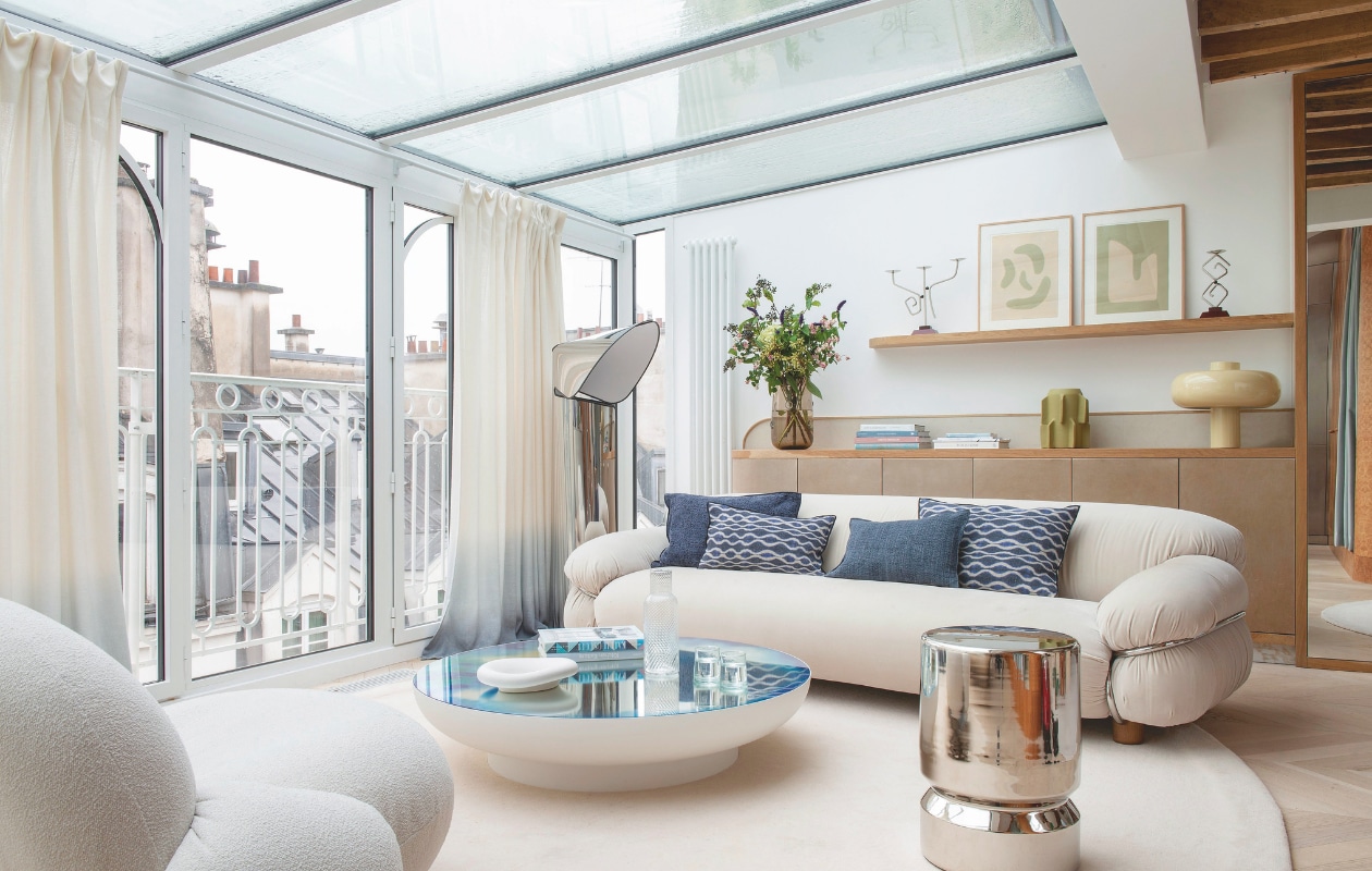 Bank Sesann van Tacchini. Kussens Maison de Vacances. Salontafel Francis van Petite Friture. Vloerlamp Chiara van Mario Bellini voor Flos. Dressoir ontworpen door Amélie Vermersch. Groene vaas Clay212. Glazen vaas Am.pm. Kandelaars Garance Vallée x Monoprix. Lamp Bureau Benjamin x Monoprix. Kunstwerk Virginie Hucher. vtwonen Design 01-2026 | fotografie Nicolas Mathéus