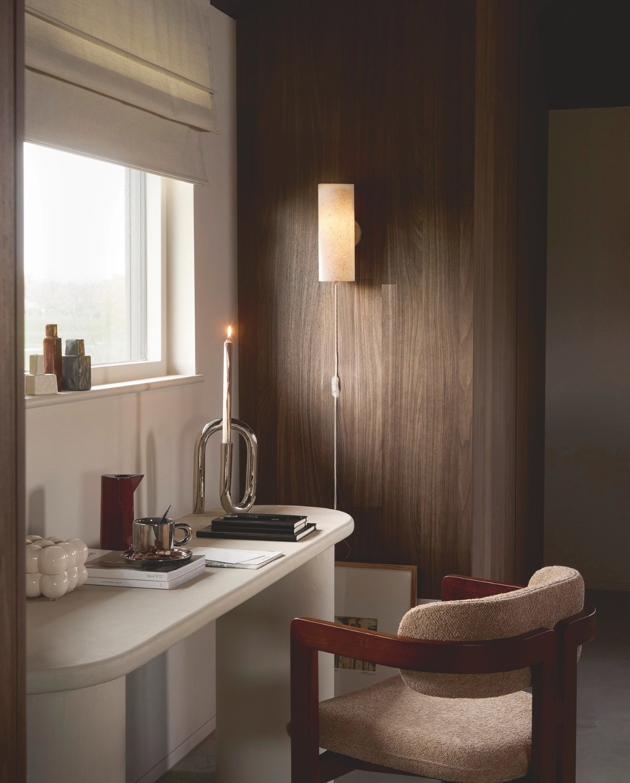 vtwonen wandlamp Paper Tube, papier, 16,5x11x30 cm (bxdxh) € 49,99.M.m.v. loods5.nl (eetkamerstoel, kop en schotel, bordeauxrode kan, kleine vaasjes, artwork, kaars), zuiver.com (chromen kandelaar, crèmekleurig opbergdoosje). Overig privébezit. vtwonen 02-2026 | styling Marlies Does | fotografie Peggy Janssen