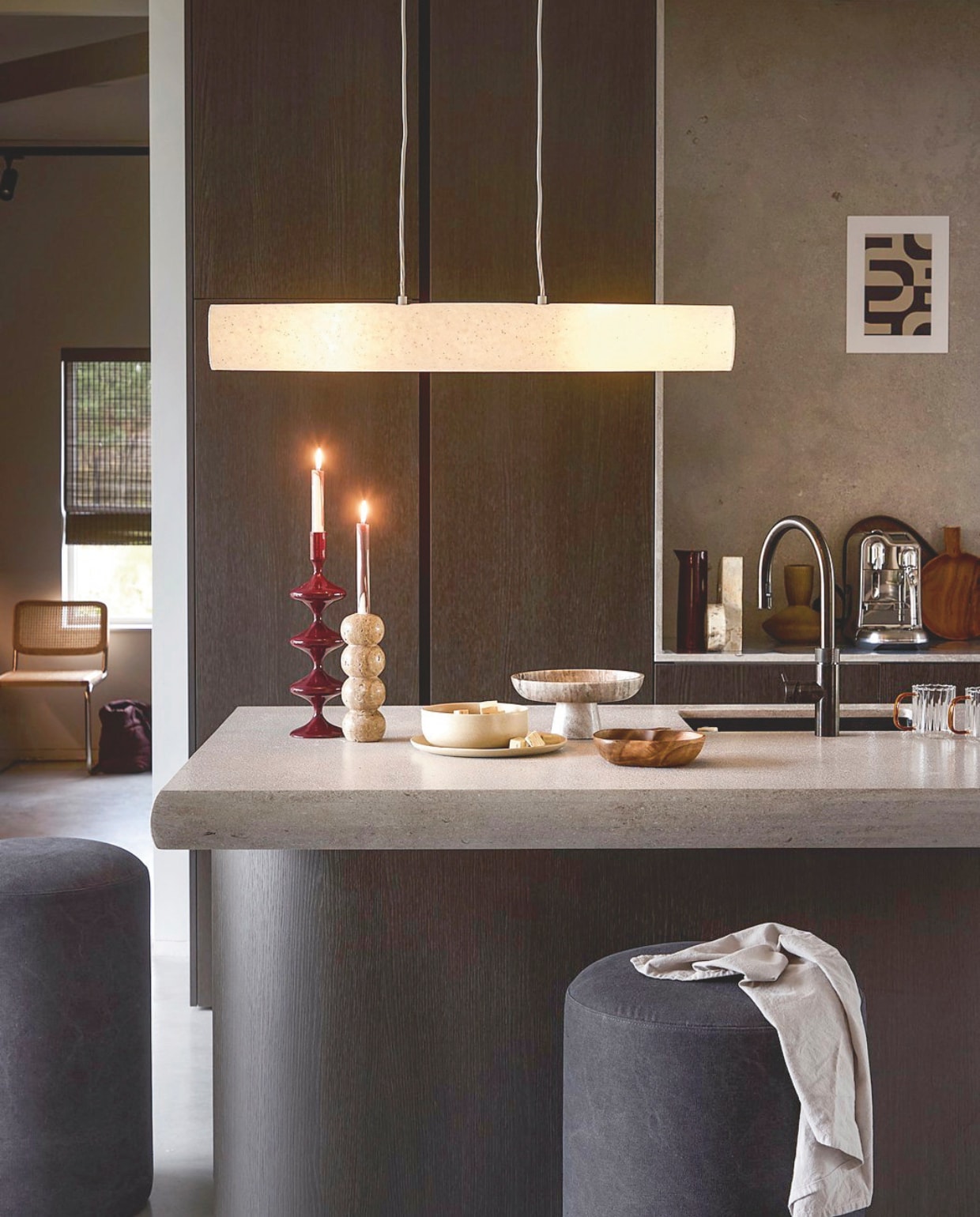 vtwonen hanglamp Paper Tube, papier, 90x11 cm (Øxh) € 149,-.M.m.v. Loods5.nl (stoel chroom en webbing, bordeauxrode kandelaar, servies, schaal op voet, houten schaal in vorm van appel, hoge kan, theedoek, bekers van glas met bruin oor, artwork, marmeren object), zuiver.com (marmeren kandelaar). Overig privébezit. vtwonen 02-2026 | styling Marlies Does | fotografie Peggy Janssen