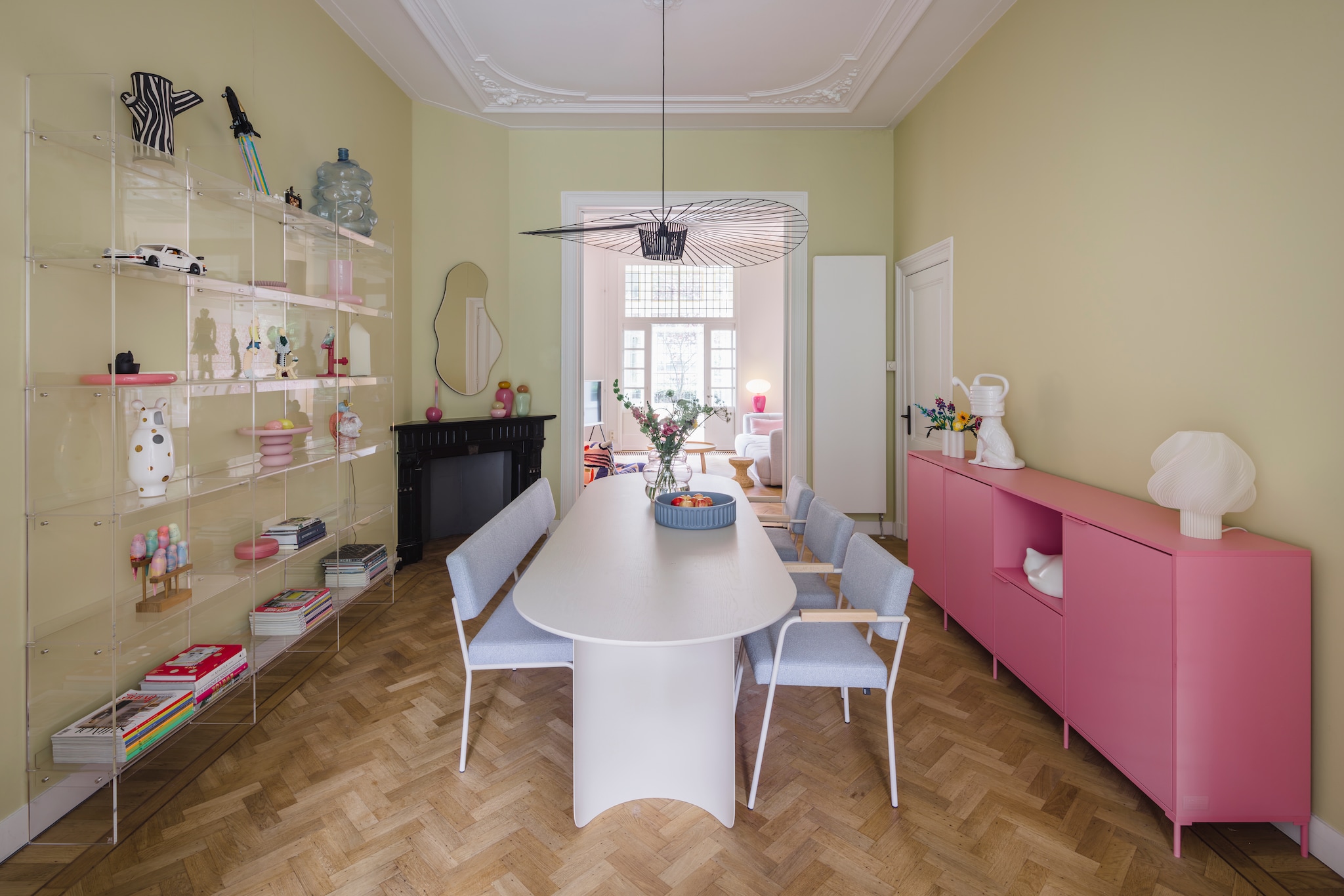 Muurkleur Lemon Tree van Little Greene. Eettafel, bank en  stoelen Fést. Dressoir Tylko. Tafellamp Crème Atelier. Lamp Vertigo van Petite Friture. Transparante kast HKliving. Parkieten Pete Cromer voor Prchtg. Spiegel Pond van Ferm Living. Glazen potten Helle Mardahl. Blauwe fruitschaal Ionic van Mae Engelgeer. Slapende kat Vitra. Hond met gieterhoofd Polspotten. Roze taartschaal Form Keramiek. vtwonen 05-2026 | styling stylestek | fotografie Eva bloem