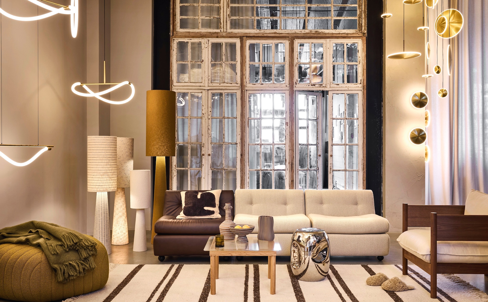 Graypants hanglamp Levity, messing, vanaf € 1200,-, wandlamp Chrona Sconce10, acrylaat en messing, vanaf € 935,- (graypants.eu). Woood tafellamp Loft, metaal en stof, naturel, 22x90 cm (Øxh) € 79,95, vloerlamp Loft, metaal en stof, olijfgroen, 35x187 cm (Øxh) € 279,-, vloerlamp Loft, naturel met strepen, naturel met stippen, 30x130 cm (Øxh) € 179,-. HKliving bijzettafel Currents, keramiek, zilver, 36x36x45 cm (lxbxh) € 158,99 (shop.vtwonen.nl). Muuto poef, groen, large, 88 cm (Ø) vanaf € 1149,- (muuto.com). Hay bank Amanta, 1-zits, gerecycled abs, leer, teddy, 79x69 cm (bxh) € 1390,-, Hay stoel Arbour Club, walnoothout, beige, 75x85x75 cm (bxdxh) € 2499,-, Hay bijzettafel Kofi, eikenhout en glas, 60x60x36 cm (lxbxh) € 519,-, HKliving gestreept vloerkleed, wol, bruin-crème, 200x300 cm (lxb) € 895,-, Ferm Living vaas Brura Coffee, keramiek, wit-bruin gestreept € 79,-, Ferm Living schaal Brura Coffee, keramiek, wit-bruin gestreept € 59,-, Ferm Living vaas Moire, steen, antraciet € 95,- (loods5.nl). Suite702 plaid, mohair, olijfgroen, 130x180 cm (lxb) € 249,95 (suite702.com). Overig privébezit. vtwonen 02-2026 | styling Marianne Lunning | fotografie Alexander van Berge