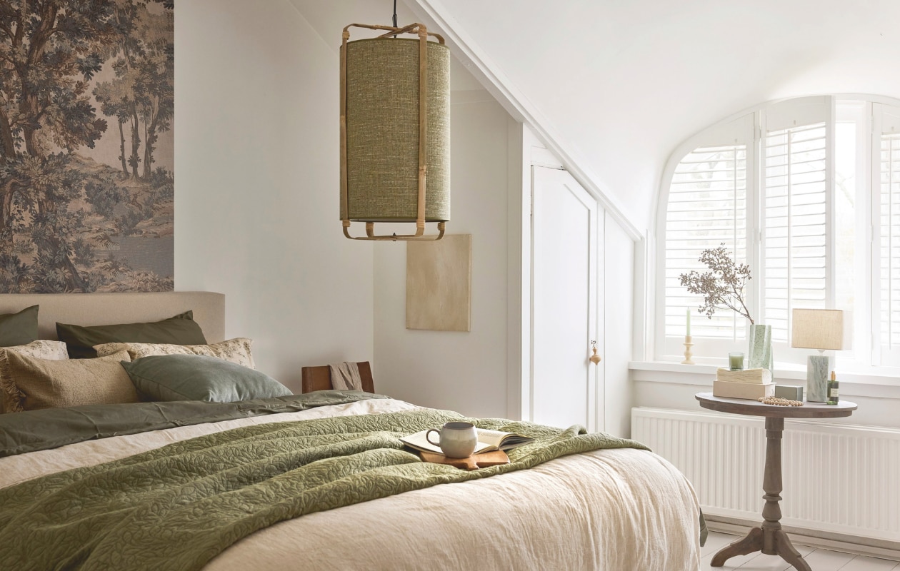 Raw Materials eetkamerstoel Freya, hout en leer, bruin, 50x45x80 cm (bxdxh) € 349,-, Light & Living hanglamp Sendai, stof en metaal, groen, 42 cm (Ø) € 199,95, Urban Nature Culture vaas Spille, keramiek, groen € 64,99 (shop.vtwonen.nl). Belartestudio behang Tapestry Landscape, beige, per m² € 55,- (belartestudio.com). Bonsoir kussen, fluweel, zachtgroen € 40,-, dekbedovertrek, katoensatijn, groen € 140,- (bonsoir.com). Zara Home dekbedovertrek, gestreepte structuur, katoen, gebroken wit € 119,-, bedsprei gewatteerd met bladeren, katoen, groen € 89,99, kussensloop bloemenprint, katoen, beige € 22,99, kussenhoes franjes, katoen, sand € 19,99, snijplank, hout, lichtbeige € 22,99, kamerjas, gewafeld linnen, beige € 119,- (zarahome.com). Schilderij, 30x40 cm (lxb), prijs op aanvraag (sanneketelaar.com). Dille & Kamille mok, steengoed, grijs € 8,50 (dille-kamille.nl). Overig privébezit. vtwonen Landelijk 02-2026 | styling Sanne Ketelaar | fotografie Alexander van Berge