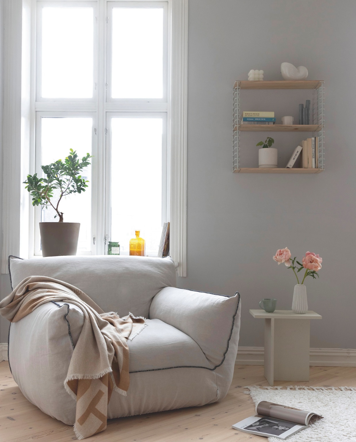 Linnen fauteuil Gia van Pastill. Bijzettafel zelf gemaakt. Wandrek Kristin van Kremmerhuset, geïnspireerd op systeem van String furniture. Nora zette gekleurd glaswerk van een rommelmarkt op de vensterbank, omdat het ’t natuurlijke licht zo mooi weerkaatst. vtwonen 01-2026 | styling Mari K. Olsen | fotografie Filippa Tredal | productie House of Pictures