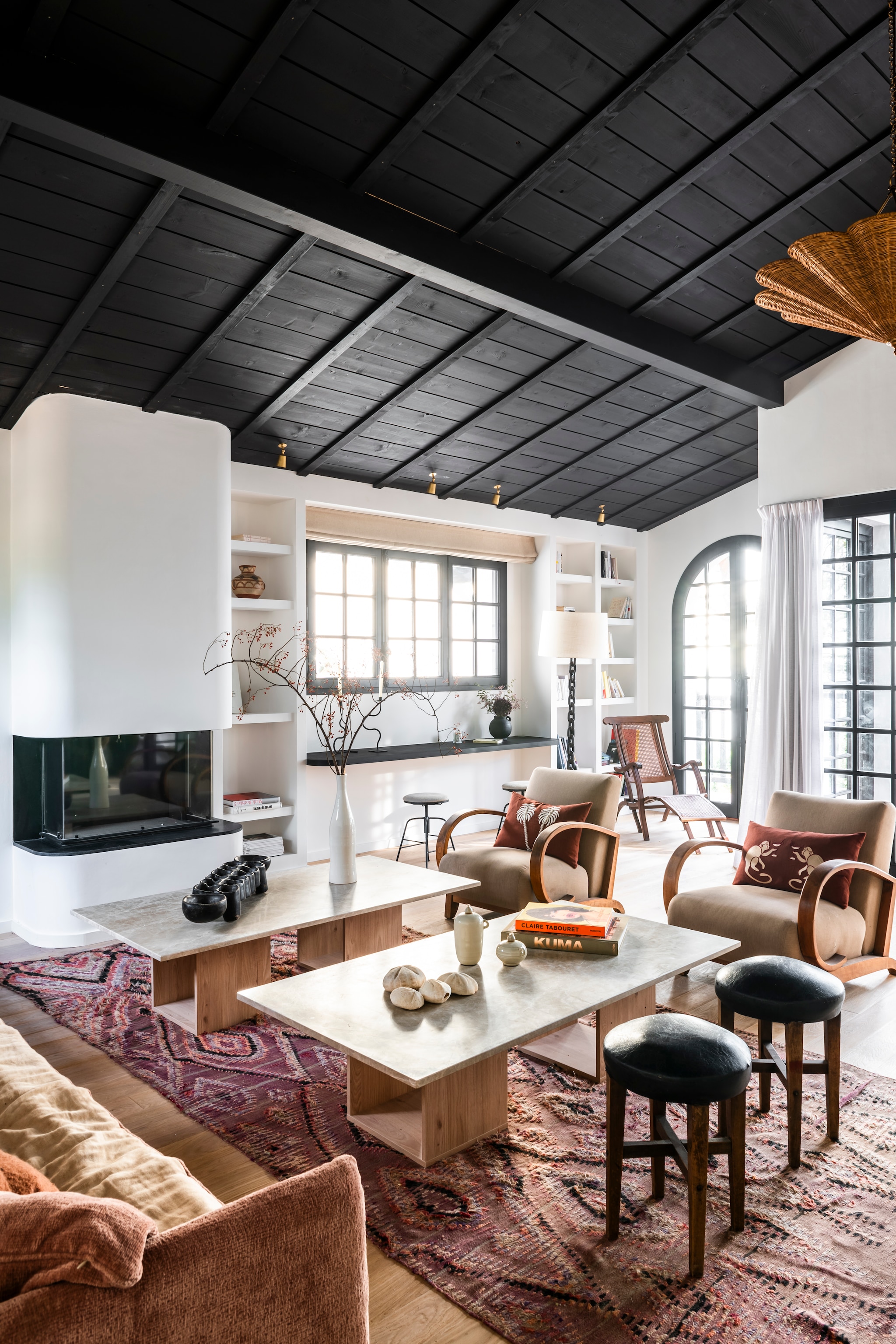 Plafond en ramen kleur Ral 8022. Muren met kalk gepleisterd. Open haard, boekenkast en salontafels van Brecha-marmer van Levantina en hout, ontworpen door Theresa. Bank Bérengère Leroy. Fauteuils uit dejaren 30. Kussens La Casano. Krukken en Afrikaans awale-spel van KokobongoArt via Etsy. Spots Corston. Vergelijkbaar vloerkleed Kilim van Louis De Poortere. Vouwgordijn Heytens. vtwonen landelijk 7-2026 | styling Amandine Berthon | fotografie Julien Fernandez | productie Amandine et Jules