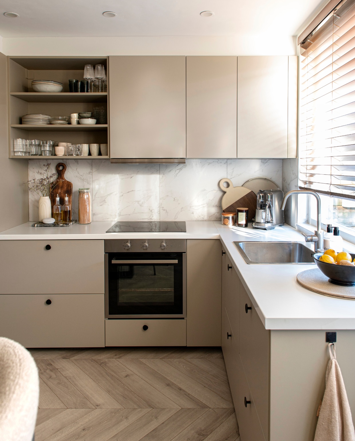 Kastfronten Havstorp van Ikea in beige, zijpanelen geverfd in NCS S 3005-Y20R, meubelknoppen Zara Home, jaloezieën Veneta. Rechthoekige serveerplank en handdoek Blokker. Vaas en fruitschaal kringloop. Speaker Google Nest. Koektrommel  en olie- en azijnset Hema. Weckpot Ikea, ronde serveerplank Gusta, dienblad  Light & Living geverfd in  NCS S 3005-Y20R, koffiemachine Nespresso Creatista. Geurkaars en placemats H&M Home. Servies in open kast van boven naar beneden en van links naar rechts: schalen Casa, glazen Iittala, wijnglazen blokker. Borden Ikea, gestapelde gebaksborden kringloop en Søstrene Grene, mokken Casa, schaal Ikea. Glazen Blokker, glazen Ikea, mokken Nespresso, organische glazen Kwantum, mokken Casa. Overig onbekend.  vtwonen 04-2024 | fotografie Caroline Coehorst | styling Jeske Weel