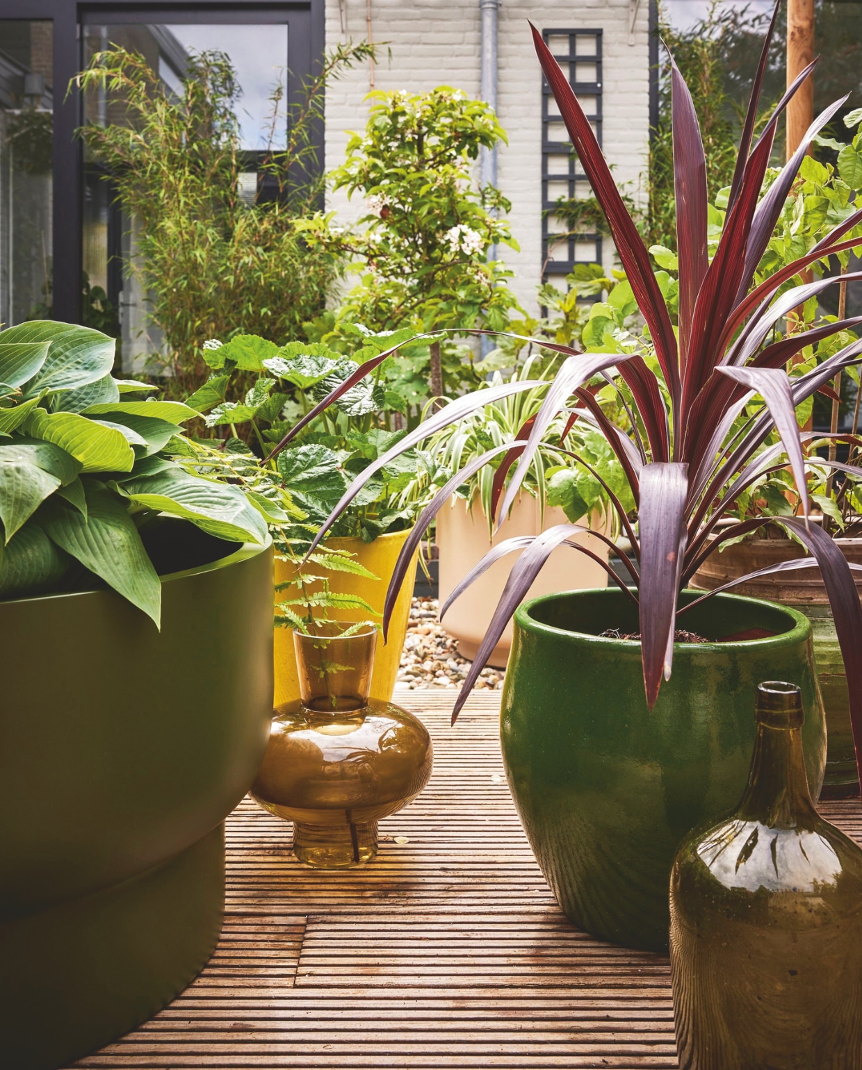 Grote groene kunststof plantenbak Nyborg van Vase the World, 40x70 cm (hxØ) € 180,99, zandkleurige pot, 30,5x35 cm (hxØ) € 41,95, olijfgroene glazen vaas van vtwonen € 44,95 (shop/vtwonen.nl). Gele en groene pot bij goed gesorteerde tuincentra. vtwonen special tuin 10 | styling Fietje Bruijn | fotografie Alexander van Berge
