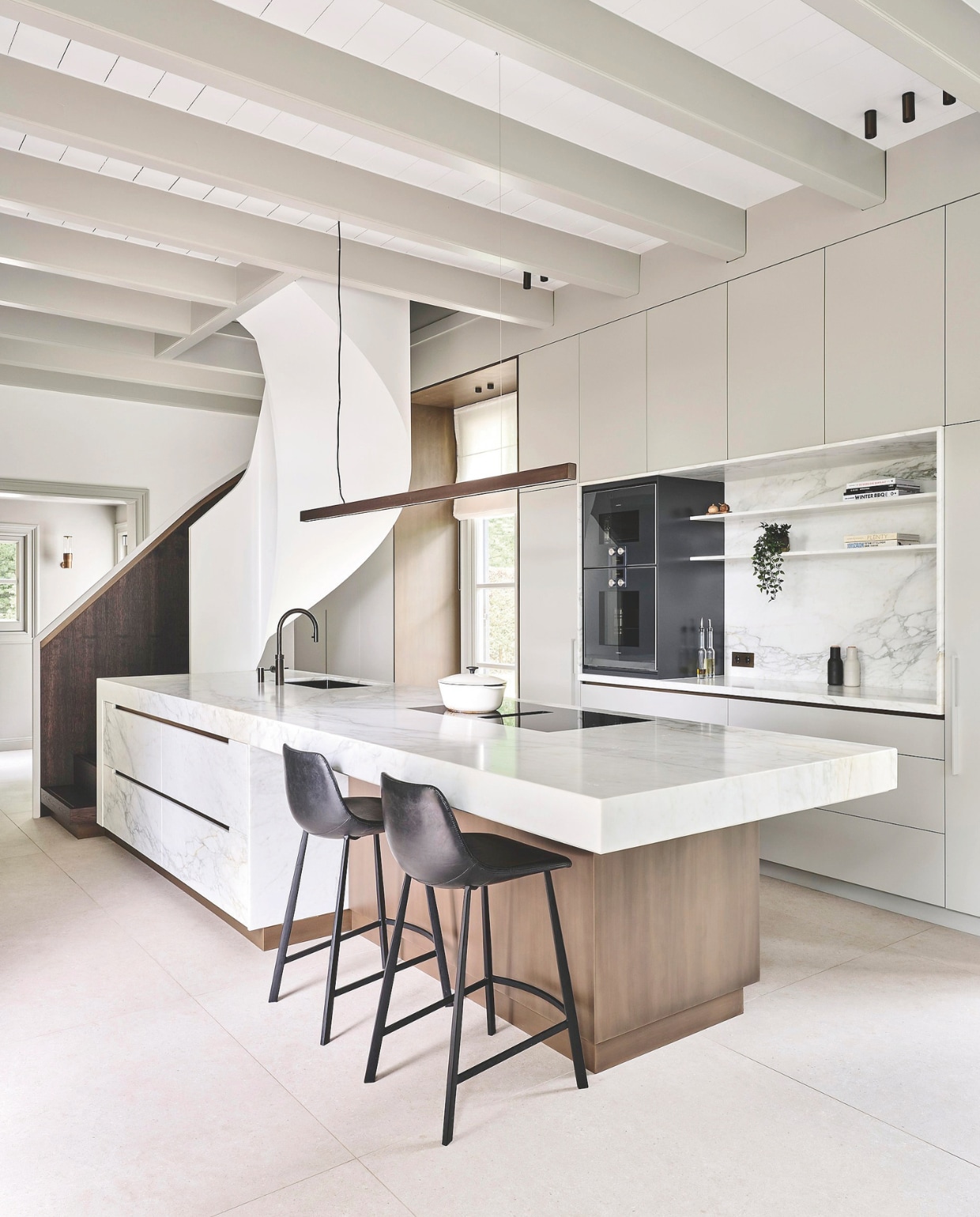 Keukenontwerp Studio Ruim, uitgevoerd door Veluwse Makers. Kookplaat Bora, blad van Arabescato marmer. Keukenkastjes gespoten in lichte bronskleur. Spots Modular. Vloer Living Ceramics. Kraan Quooker. Trapontwerp Studio Ruim. Lamp boven kookeiland Studio Rublek. Wandlamp Viabuzzono. Vouwgordijnen Siersema Stoffeerders.  vtwonen 01-2026 | fotografie Space Content Studio