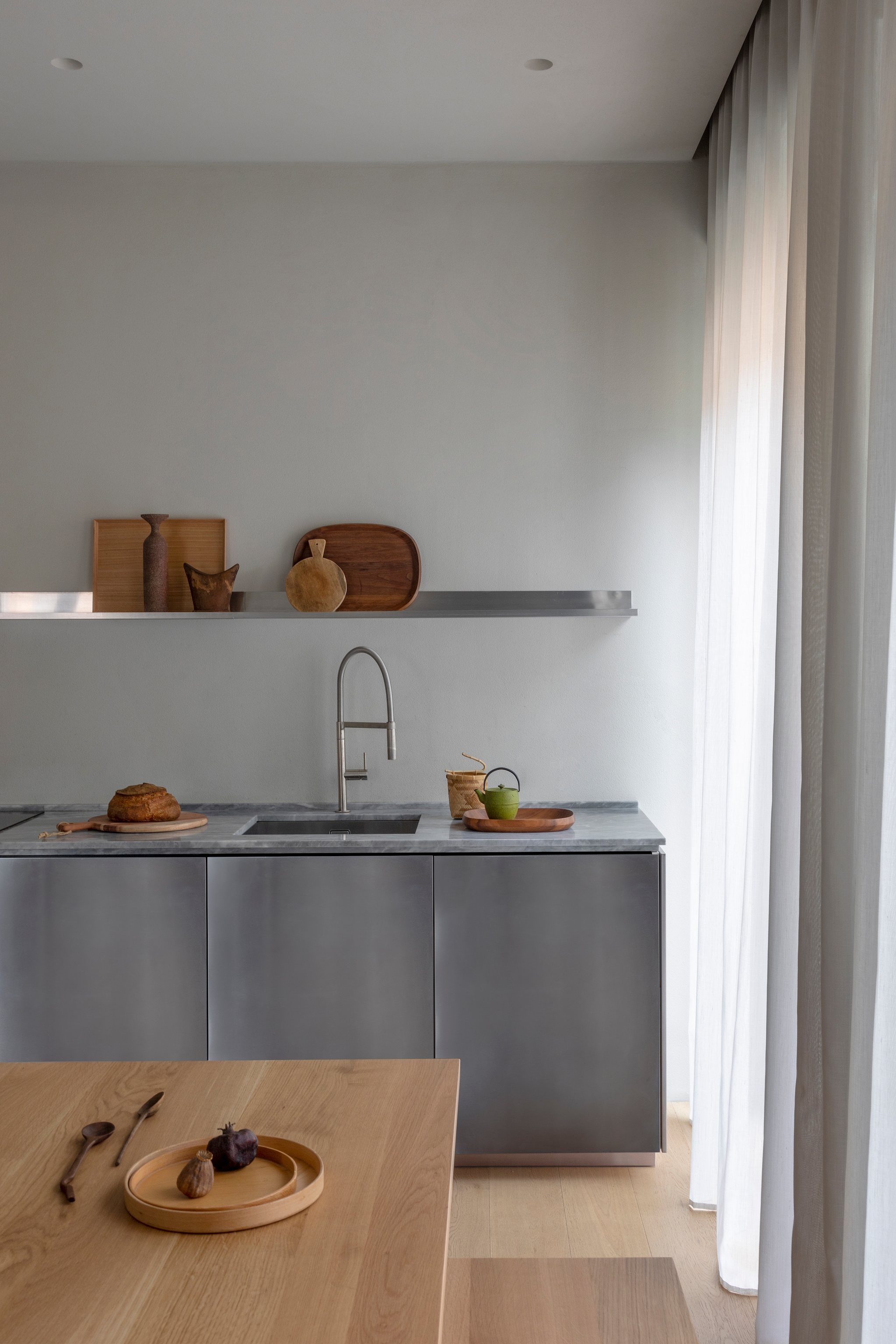 De keuken van roestvrij staal en marmer is een ontwerp van Moreno en bevindt zich in de woonkamer. Op het schap: keramiek van Milesi, Afrikaanse hoofdsteun, ovale houten tray van Federica Biasi voor Coin. vtwonen Design 04-2026 | styling Chiara Dal Canto | fotografie Helenio Barbetta | productie Living Inside