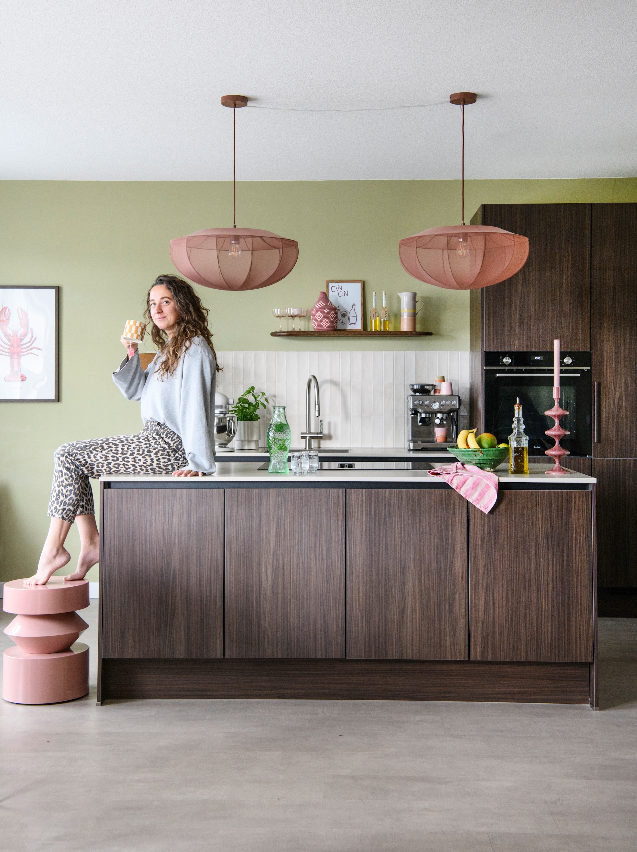 Muurverf Puur Helmgras van Flexa. Keuken Keukenconcurrent. Wandtegels Tegels in huis. Hanglampen Westwing. Wandplank By-Boo. Glazen, theedoek, fruitschaal, kandelaar en lamp met houten voet Loods5. Roze mand Studio Bohome. Karaf HKliving. Schilderij op wandplank zelfgemaakt. Olieflessen kringloop. Glazen fles vis Serax. vtwonen 06-2026 | styling Maaike van Haaster | fotografie Louis Lemaire | productie Insidehomepage