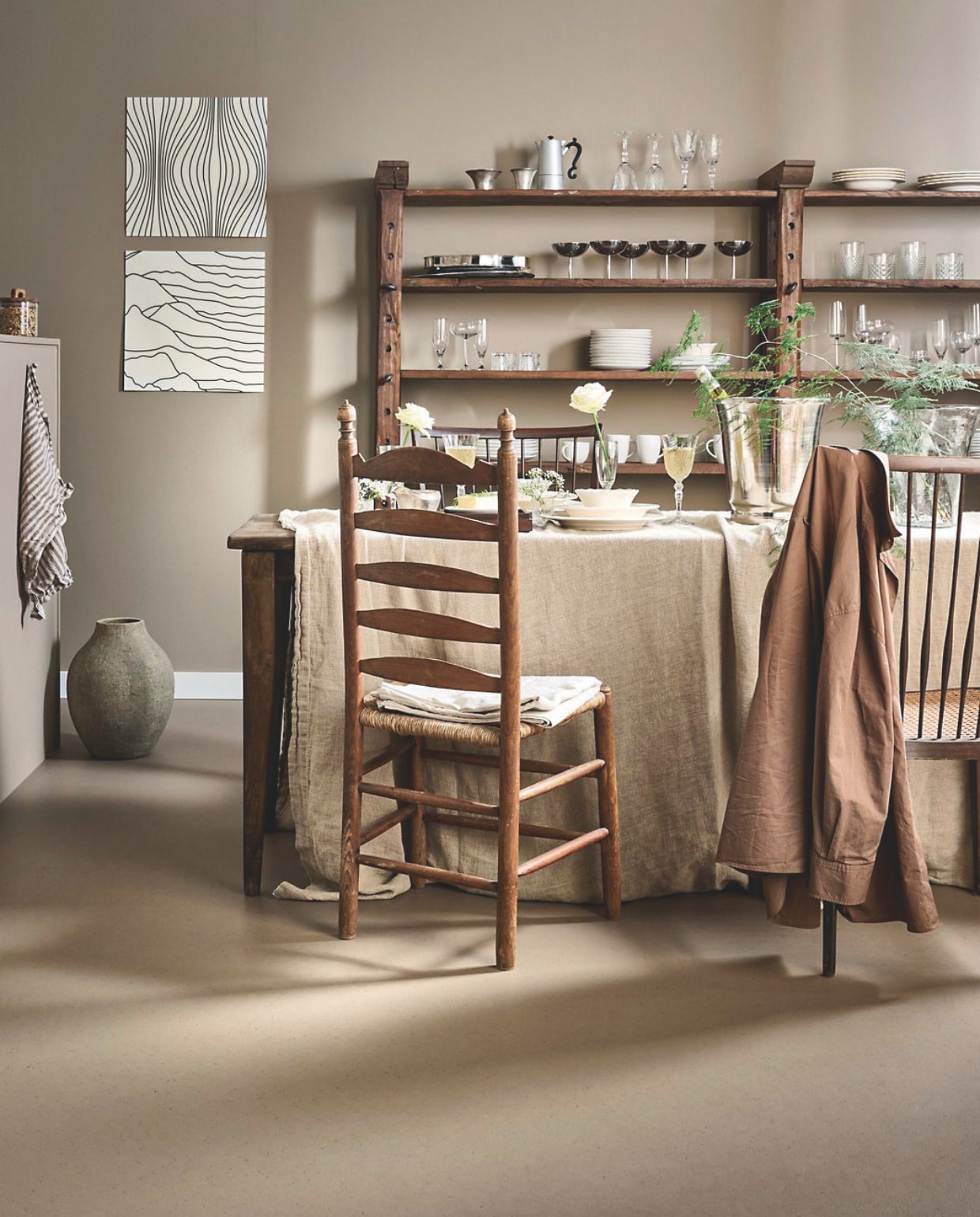 vtwonen Marmoleum Cocoa, leem, 200 cm breed, per m² € 53,80.M.m.v. defransetafel.nl (tafel), com-anders.nl (stoelen, kast), zarahome.com (aardewerken vaas, glazen vaas, wijnkoeler, peper-en-zoutstel, wijnglazen), vtwonen.nl (longdrinkglazen van vtwonen rechts boven in kast, wit servies van vtwonen). Overig privébezit. vtwonen Landelijk 02-2026 | styling Kim van Rossenberg | fotografie Sjoerd Eickmans
