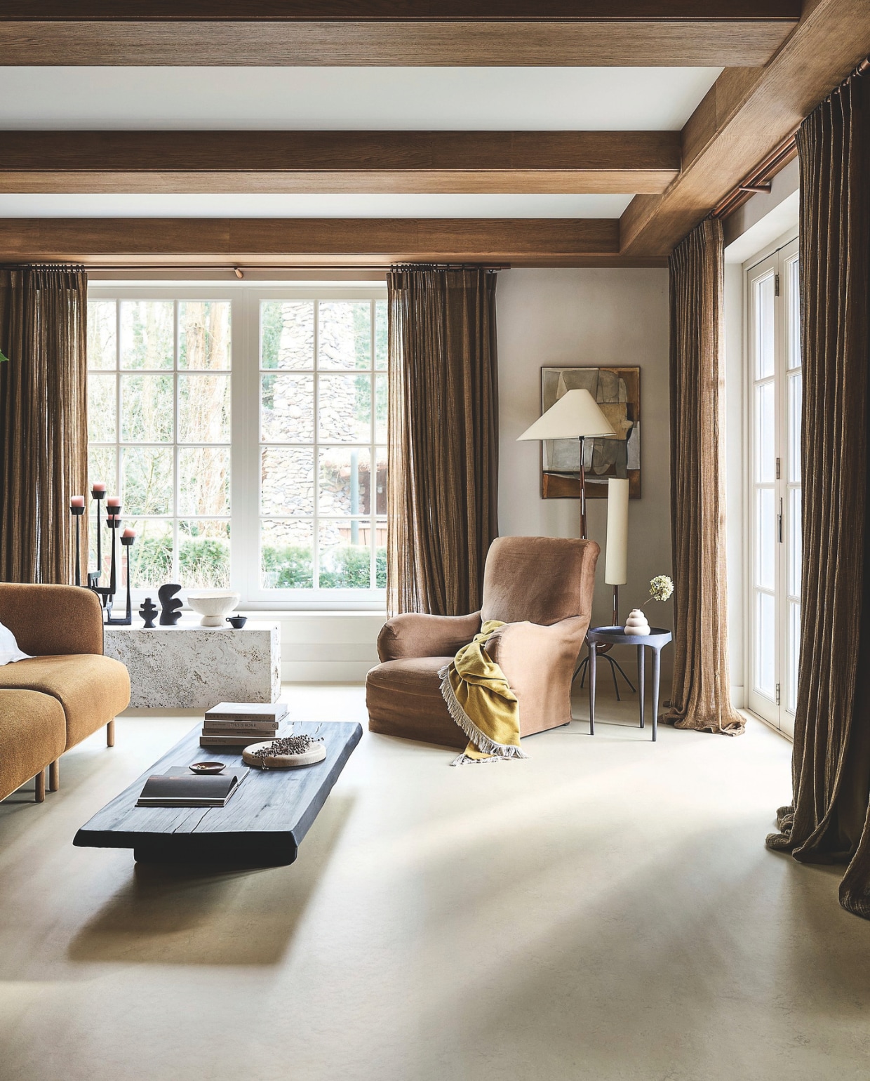 vtwonen Marmoleum Marble, almond,200 cm breed, per m² € 53,80.M.m.v. demachinekamer.nl (bank), cassina.com (fauteuil), wdstck.eu (salontafel), 101cph.com (bijzettafel), zarahome.com (witte schaal, kussenhoes, travertin schaal, zwart potje, bruin schaaltje), woood.nl (kandelaar), fermliving.com (zwarte organische vazen), ilsevanstoltz.com (wandkunstwerk Naive). Overig privébezit. vtwonen landelijk 02-2026 | styling Kim van Rossenberg | fotografie Sjoerd Eickmans