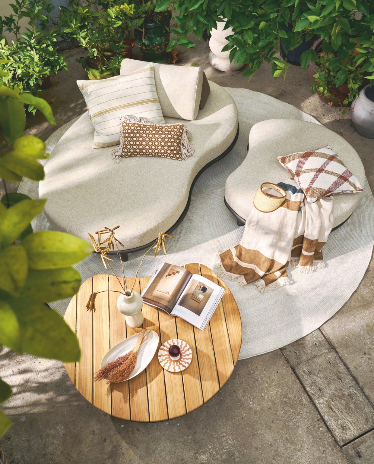 Apple Bee sofa Moon Island, olefin-stof en gepoedercoat aluminium frame, zandtint, 196x110x81 cm (lxbxh) € 1449,-,  poef Moon Island, 110x90x40 cm (lxbxh) € 669,-, salontafel Moon Island, gepoedercoat aluminium en teakhout, 110x97x24 cm (lxbxh) € 799,-, buitenkleed Swirl,  gerecycled pet, zand, 300 cm (Ø) € 759,- (applebee.nl). Omar buitenkussen Oxy, fijn gestreept, crème-bruin, inclusief vulling € 195,-, buitenkussen Oman, geruit, inclusief vulling € 165,-, kussen Odile met franjes, bruin-crème, fijne ruit, inclusief vulling € 165,- (omar-antwerp.be). Libeco deken Julian, linnen € 396,- (libecohomestores.eu). Household Hardware vaas Bubble, tadelakt € 115,-, bord Fez, keramiek € 15,-, Woood bijzettafel Laurel, magnesium, spikkels beige, 50x40x40 cm (lxbxh) € 99,95 (shop.vtwonen.nl). Overig privébezit.