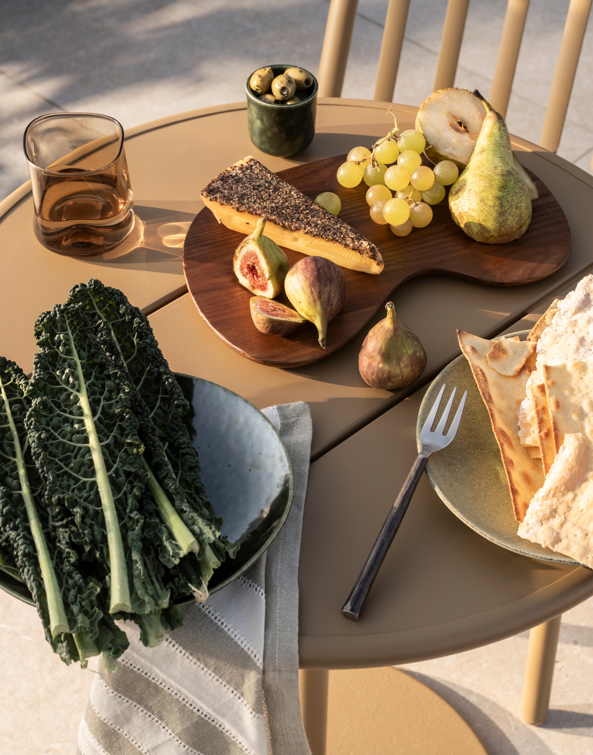 Fatboy tafel Fred’s Bistreau, aluminium, metaal, bruin, 60x76 cm (Øxh) € 399,-, tuinstoel Fred’s, aluminium, metaal, bruin, 52x56x80,5 cm (bxdxh) € 269,- (fatboy.com). Ferm Living snijplank Cairn, essenhout, donkerbruin, set van 3 € 139,- (fermliving.com). Gommaire bestekset roestvrij staal, zilver, 5-delig € 51,- (gommaire.com). Zara Home servet met kant, katoen en linnen, groen en wit € 9,99 (zarahome.com). Leonardo drinkglas, bruin, transparant € 12,95 (debijenkorf.nl). H&m Home borden, keramiek, groen, set van 4 € 39,99, espressokopjes, keramiek, groen, set van 4 € 19,99,  (hm.com). Overig privébezit. vtwonen Special 02-2026 | styling Sanne Ketelaar | fotografie Stan Koolen