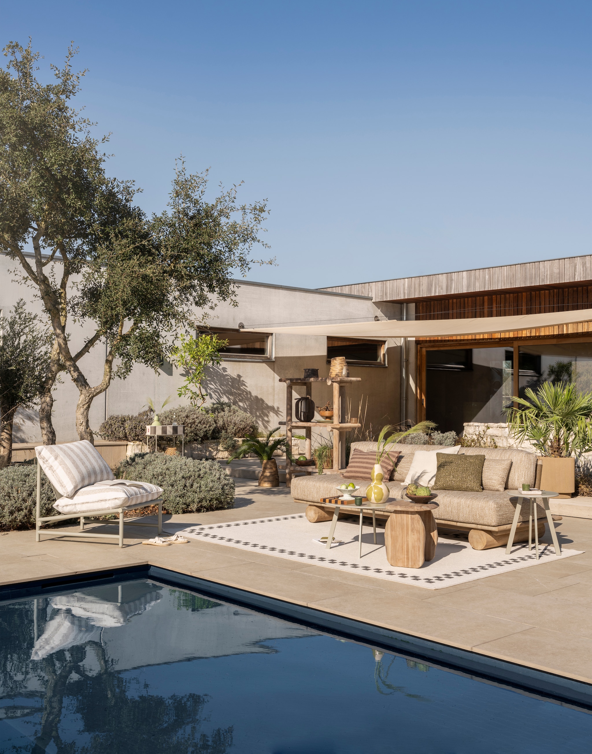 Woood loungestoel Elvo Tuin, aluminium, wit en zand, 82x75x75 cm (bxdxh) € 249,-, bijzettafel Fer Tuin, metaal, zand, 40x49 cm (Øxh) € 34,95, bijzettafel Fer Tuin, metaal, zand, 70 cm (Ø) € 64,95 (shop.vtwonen.nl). Gommaire bank Sofa Edge, teakhout, naturel 240x100x70 cm (bxdxh) € 3475,-, kussenset Sofa Edge, outdoor stof, sneldrogend schuim, beige en grijs € 2735,-, kast Rolf, teakhout, naturel, 120x40x50 cm (lxbxh) € 2395,-, pot Melda, terracotta, goudbruin € 75,-, mand Nest, wicker en pitriet, naturel, klein € 50,-, groot € 60,- (gommaire.com). Fatboy rek Adoreganizer, metaal, kunstof, wit en beige 65,5x29x76,5cm (lxbxh) € 219,-, buitenvloerkleed Carpretty grand, polypropyleen, beige en zwart, 300x200 cm (lxb) € 299,- (fatboy.com). Ferm Living snijplank Stripe Bold, walnoot en eikenhout, naturel en bruin € 139,-, dienblad Mist, hars en kunststof, parel € 29,- (fermliving.com). HKliving schaal op voet New Classics, aardewerk, lichtblauw, 20 cm (Ø) € 44,95 (hkliving.com). Zara Home vaas met bloemen, terracotta, groen € 39,99, gestreepte kussenhoes, katoen, bruin € 39,99, kussenhoes met structuur, katoen, lichtgroen € 15,99, vaas, geëmailleerd terracotta, turquoise € 39,99 (zarahome.com). H&m Home rotan schaal op voet, naturel € 29,99, espressokopje, keramiek, groentinten, set van 4 € 19,99, espadrilles met gedraaid detail, katoen en rubber, beige € 14,99, decoratief potje, keramiek en glas, amber € 12,99 (hm.com). Overig privébezit. vtwonen Special 02-2026 | styling Sanne Ketelaar | fotografie Stan Koolen