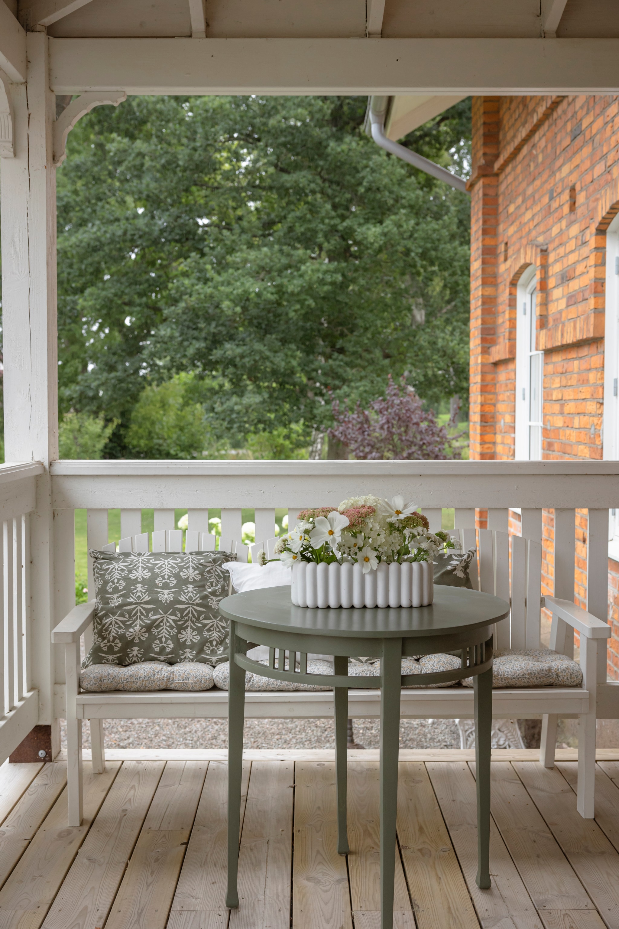 Bank Ellos. Tafel van de veiling, geschilderd in kleur Herregård Grønn van Jotun. Stoelkussens Jysk. Sierkussens H&m. Potten Lilla Stenhuset. vtwonen Landelijk 06-2026 | styling Anna Bjelkholm | fotografie Anna Karlsson
