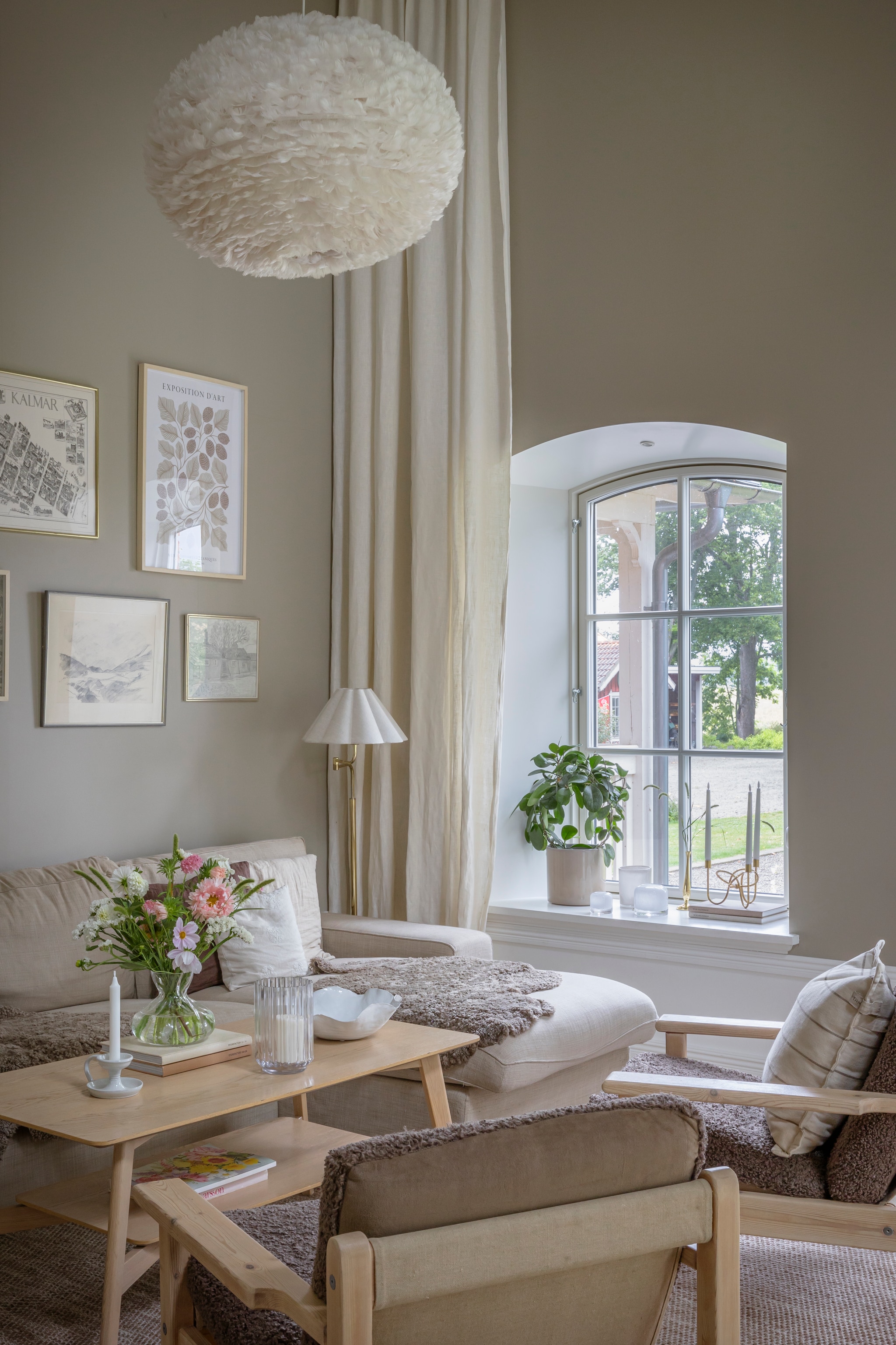 Muurverf s3005-y20r van Jotun. Bank Kivik van Ikea. Kussens, plaid en schaal Lilla Stenhuset. Stoelen veiling, zelf geschuurd en opnieuw bekleed.  Gordijnen zelf gemaakt van stof van Ikea. Hanglamp Eos van Umage. Wandkunst Desenio, zelf gemaakt, vlooienmarkt en geërfd. Salontafel, vloerlamp, kandelaar en vaas vlooienmarkt. Vloerkleed Mio. Windlicht Åhléns. In vensterbank: bloempot en kandelaar Lilla Stenhuset. Kaarsen Svenskt Tenn. vtwonen Landelijk 06-2026 | styling Anna Bjelkholm | fotografie Anna Karlsson