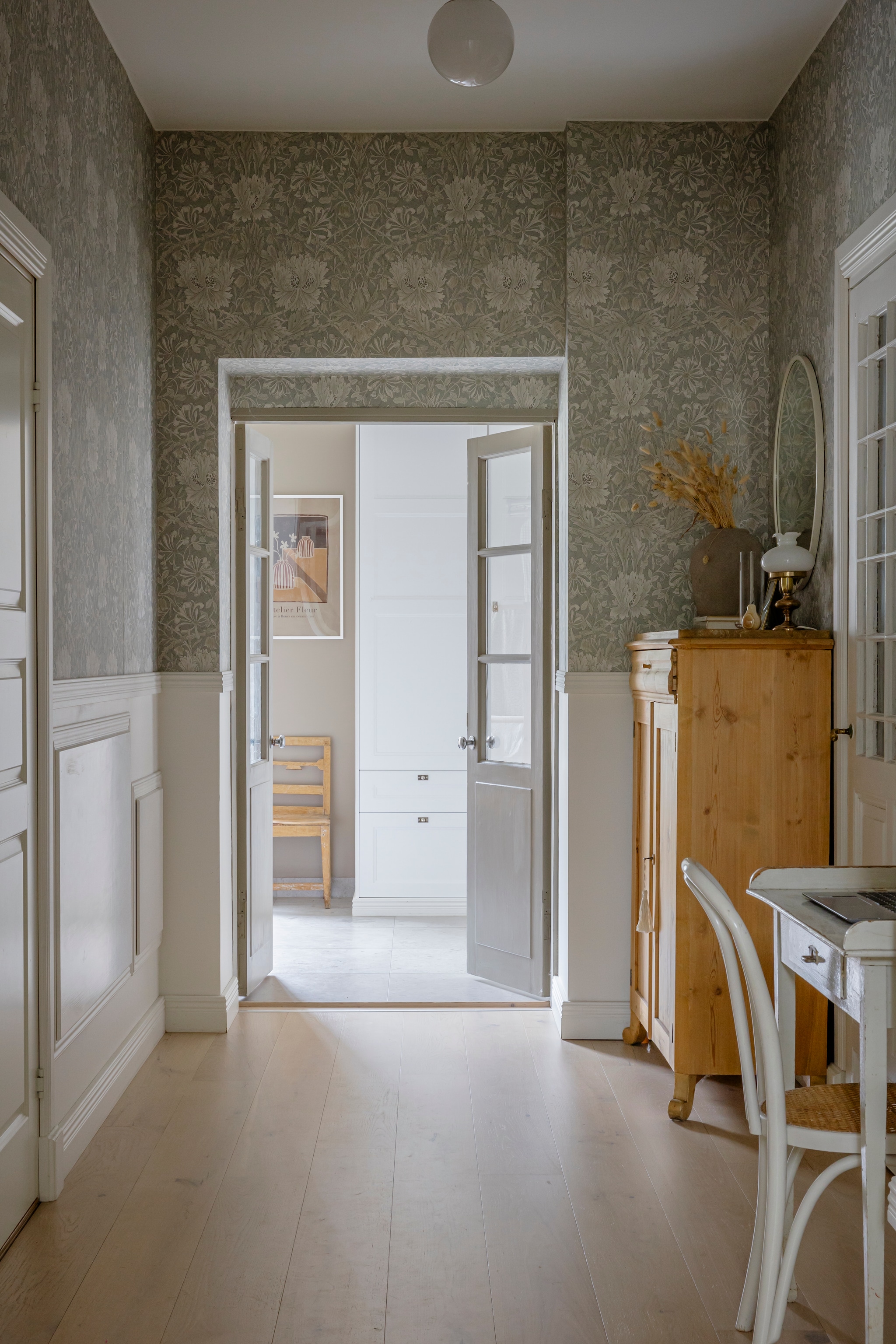 Behang Pure Honeysuckle & Tulip Grey Blue van Morris & Co. Vloer gewit eiken van Bjelin. Bureau veiling. Kast, spiegel, lamp, vaas, bureau en stoel kringloop. vtwonen Landelijk 06-2026 | styling Anna Bjelkholm | fotografie Anna Karlsson