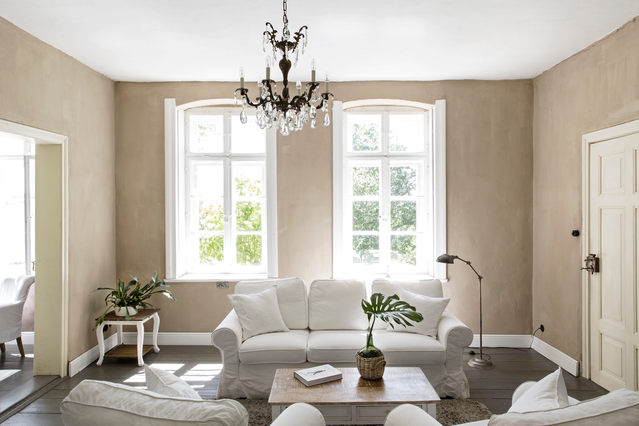 Bank en fauteuils Ikea. Kroonluchter antiek. Salontafel, bijzettafel en staande lamp Loberon. Op de muur kalkverf zelf gemengd met pigment, beide Kreidezeit. Vloerverf Disbon 404 van Caparol, gemengd in de oorspronkelijke kleur van de vloer. vtwonen Landelijk 06-2026 | styling Miriam Hannemann | fotografie André Reuter