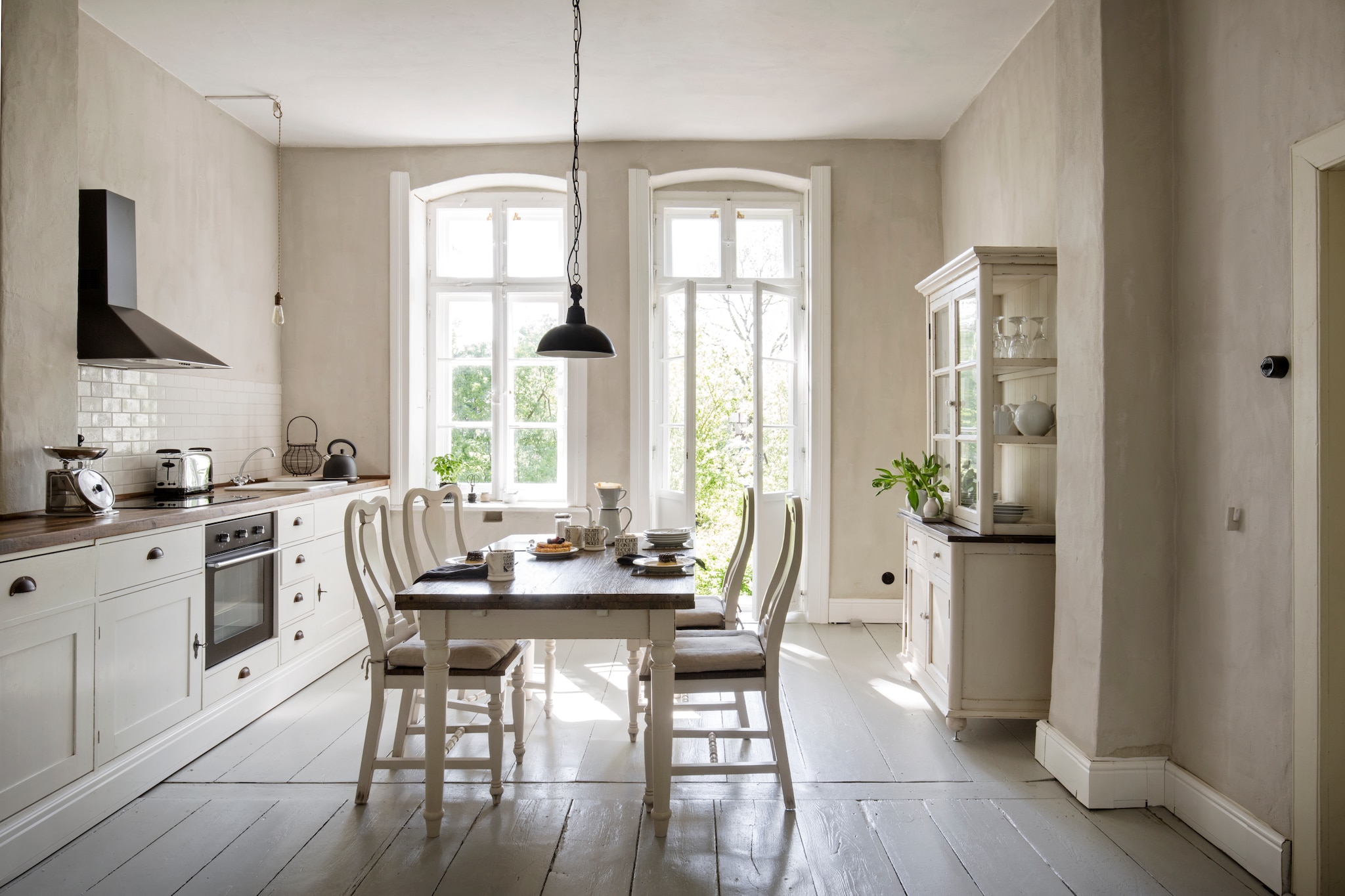 Keuken zelf ontworpen, op maat gemaakt door Old Basics. Afzuigkap Ikea. Lichtschakelaar Thpg. Eettafel, stoelen, hanglamp en servieskast Loberon. Peertjeslamp zelf gemaakt. Op de muur kalkverf, zelf gemengd met ecologisch pigment, beide Kreidezeit. Vloerverf Disbon 404 van Caparol, gemengd in de oorspronkelijke kleur van de vloer. vtwonen Landelijk 06-2026 | styling Miriam Hannemann | fotografie André Reuter