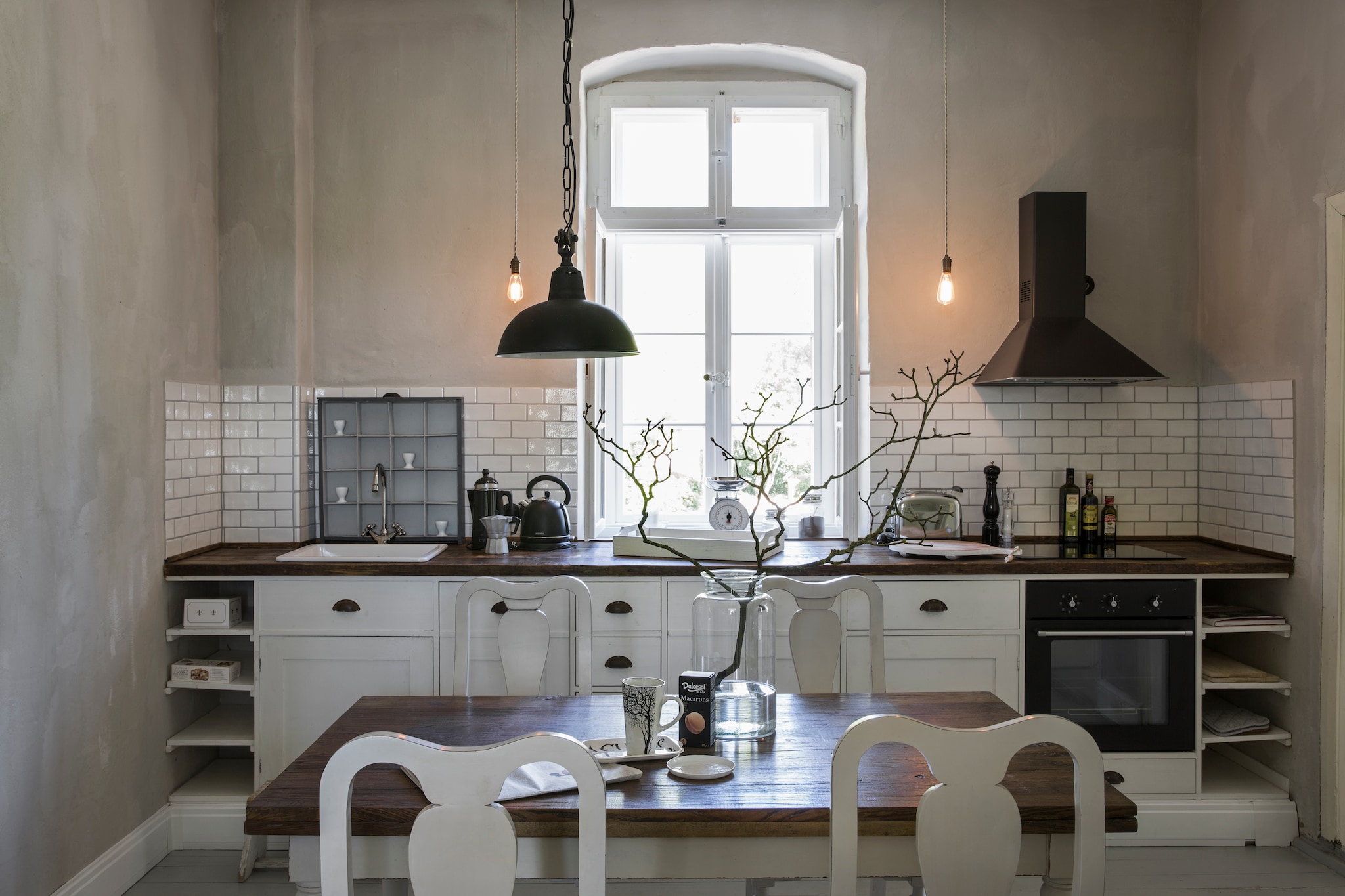 Keuken op maat gemaakt door Old Basics, inclusief het aanrechtblad van oud hout, naar ontwerp van Volker. Fornuis en afzuigkap Ikea. Letterbak achter wasbak vintage. Tafel, stoelen en hanglamp Loberon. Peertjes-lampen zelfgemaakt. Op de muur kalkverf zelf gemengd met ecologisch pigment, beide Kreidezeit. vtwonen Landelijk 06-2026 | styling Miriam Hannemann | fotografie André Reuter