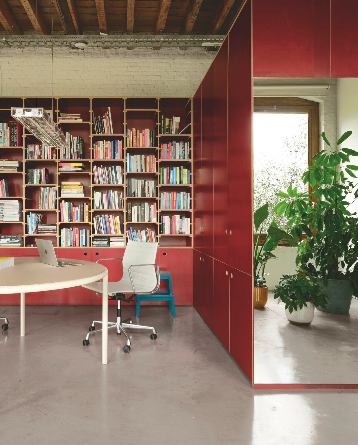 Een originele boekenkast in het sprekende rood achter de werkhoek. Bureaustoel van Eames voor Vitra. Tafel Muller Van Severen.

 vtwonen design 02-2026 | Fotografie Mr. Frank