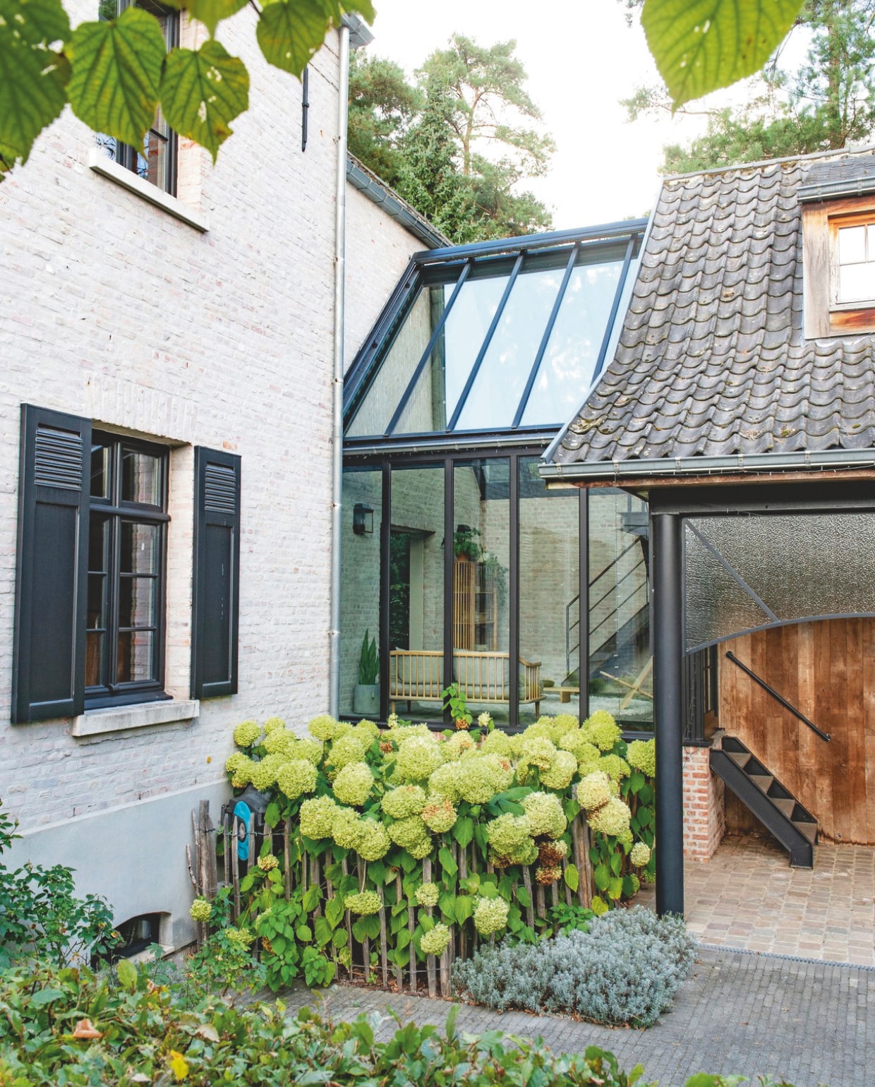 Tuin met zicht op de serre. Verfkleur kozijnen Gitzwart, gemengd bij Colora. Planten in voorste border lavendel. Planten in border tegen de serre sneeuwbalhortensia ‘Annabelle’. vtwonen landelijk 03-2026 | styling Katleen Willaert | fotografie Caroline Coehorst