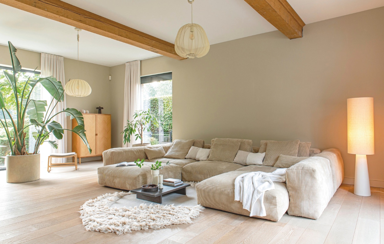 Muurkleur Buttercream Beige, gemengd bij Colora. Gordijnen Anais 10 van Qurtinz. Hanglampen Bolia. Stalamp HKliving. Bank Cord velours-sand van Vetsak. Sierkussens en sprei Zara Home. Kleed en salontafel Ferm Living. Plantsoorten Strelitzia Nicolai en Ficus. Potten Elho Pure Cilinder en Serax. Kruk Gazzda Dedo. Kast Hübsch. Bruine lamp Serax. vtwonen landelijk 03-2026 | styling Katleen Willaert | fotografie Caroline Coehorst