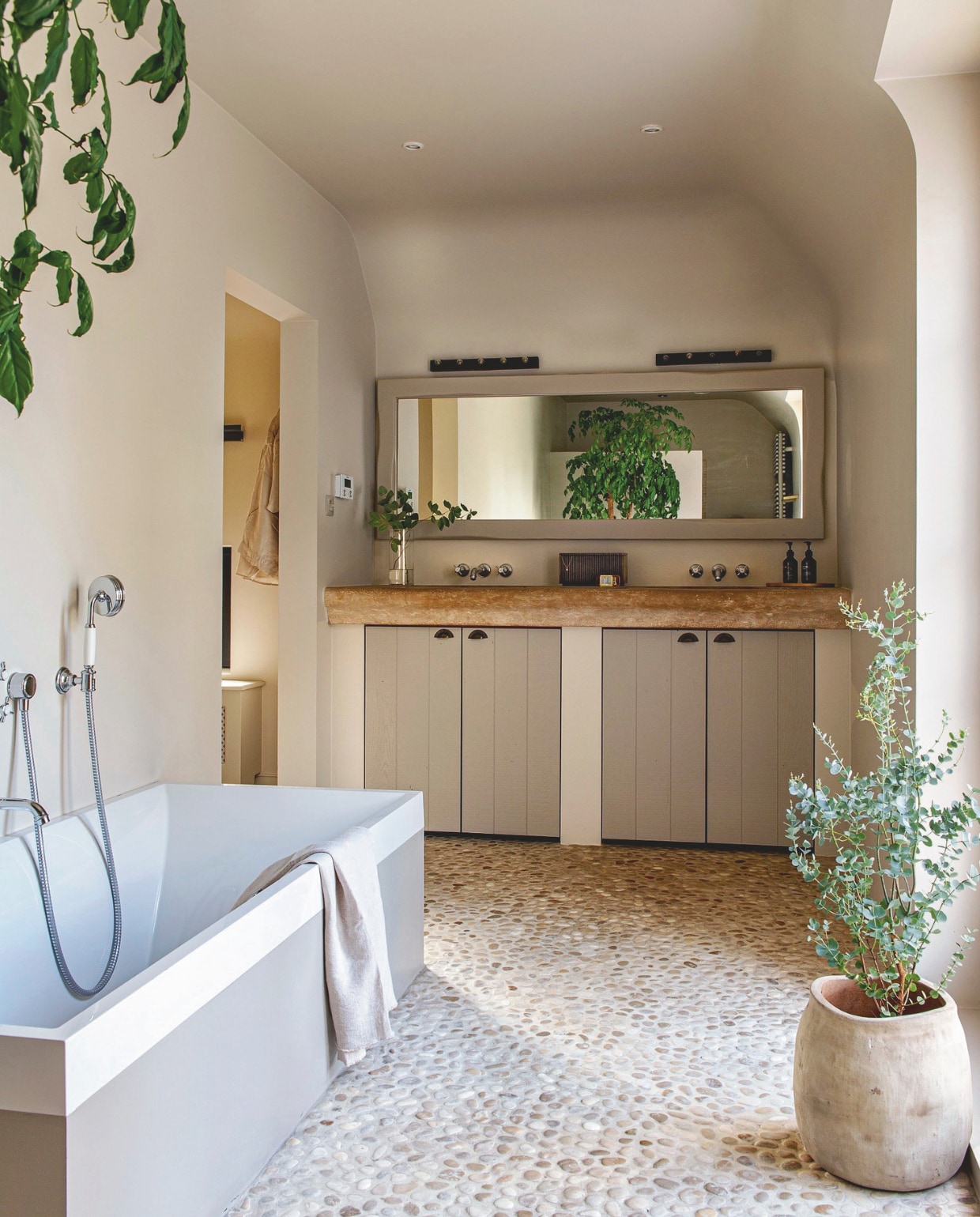 Muurkleur Skimming Stone, gemengd bij Colora. Vloer Natural Stone Mosaic. Bad Villeroy & Boch. Wandlampen Trio Leuchten Theatro. Juwelendoos H&m Home. Handdoek Zara Home. Plantensoort eucalyptus. vtwonen landelijk 03-2026 | styling Katleen Willaert | fotografie Caroline Coehorst