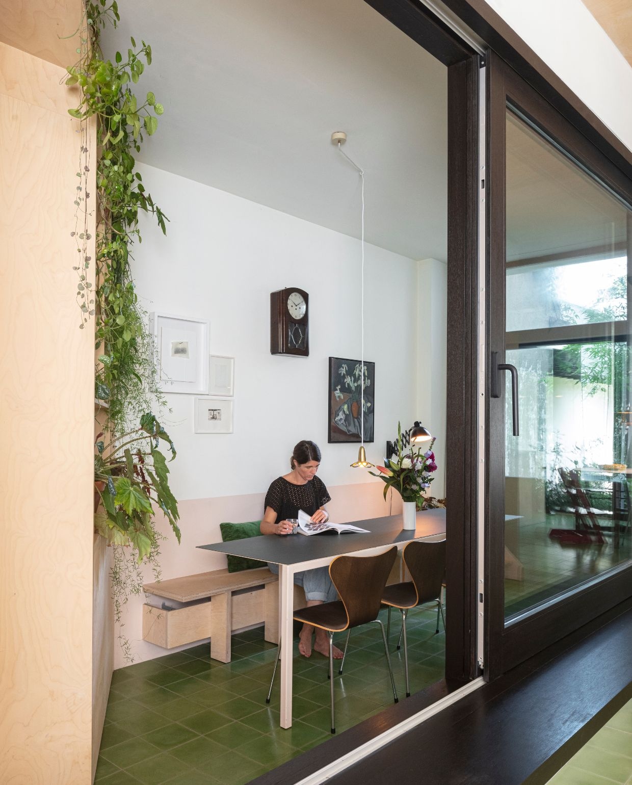 Groene cementtegels De Rocker Gent. Tafel Atelier Janda Vanderghote. Vlinderstoel Fritz Hansen Series 7 eikenfineer van Arne Jacobsen. Lamp Marguerite van Atelier Areti. Wandlamp en wandklok rommelmarkt. Stilleven Laurens Janda (Indra’s grootvader).