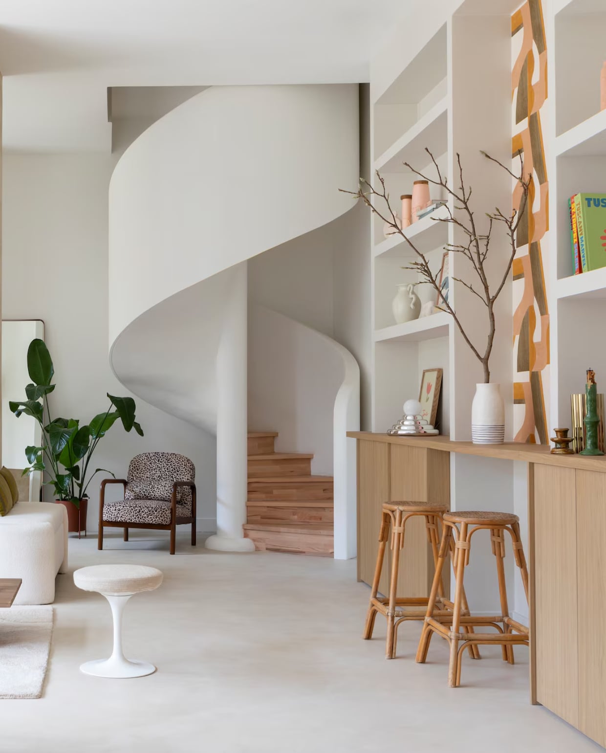 Staken trapstructuur, gipsen omkasting en beukenhouten treden Rouveure Márquez. Betonvloer en schouw Tlmt. Muurverf Porcelaine van Ressource Peintures. Inzethaard Flammes et Créations. Kasten Unilin. Terra vaas, witte vaas, spiegel, dienblad en vaas met tak H&m Home. Pot en kaars Les composantes. Tv The Frame van Samsung. Tapijt en bank Westwing. Salontafel Zara Home. Vintage Knoll-kruk, zijdespoelen en barkrukken vlooienmarkt Les Puces du Canal. Plaids Maison de vacances. Kussens HKliving. Fauteuil Sweeek. Linnen gordijnen Élitis. Behang Gino van Casamance. Chromen lamp van Axel Chay voor Monoprix. Witte vaas op plank Ferm Living. vtwonen 01-2026 | styling Marie Maud Levron | fotografie Pierrick Verny | productie AC Scoffoni