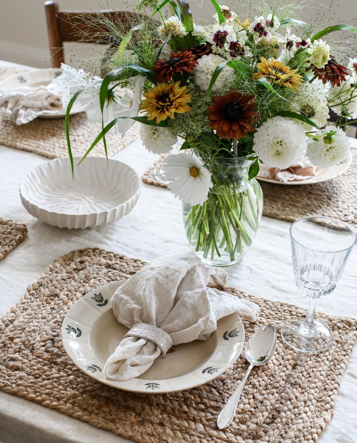 Placemat Ellos. Borden, glaswerk en vaas tweedehands. Bestek erfstukken van Sofies grootouders. Servetten en kom H&m home. Keramieken servetring handgemaakt door Johannes’ moeder. Bloemen uit de tuin: dahlia, siergras, cosmos, Ammi majus, zonnehoed enzinnia. vtwonen Landelijk 03-2026 | fotografie Rebecca Martyn