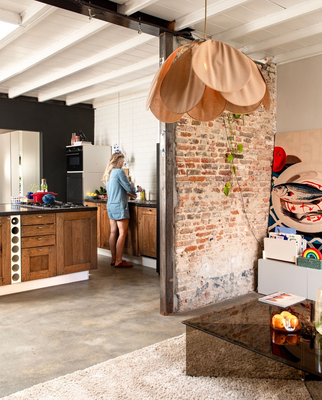 Keuken met Belgisch hardstenen werkblad en ovens van Gaggenau via Marktplaats. Theepot Le Creuset. Rode pan Lidl. Blauwe fruitschaal Hema. Plafondlamp Georges Store. Kunstwerk is een kleed bevestigd op hout.