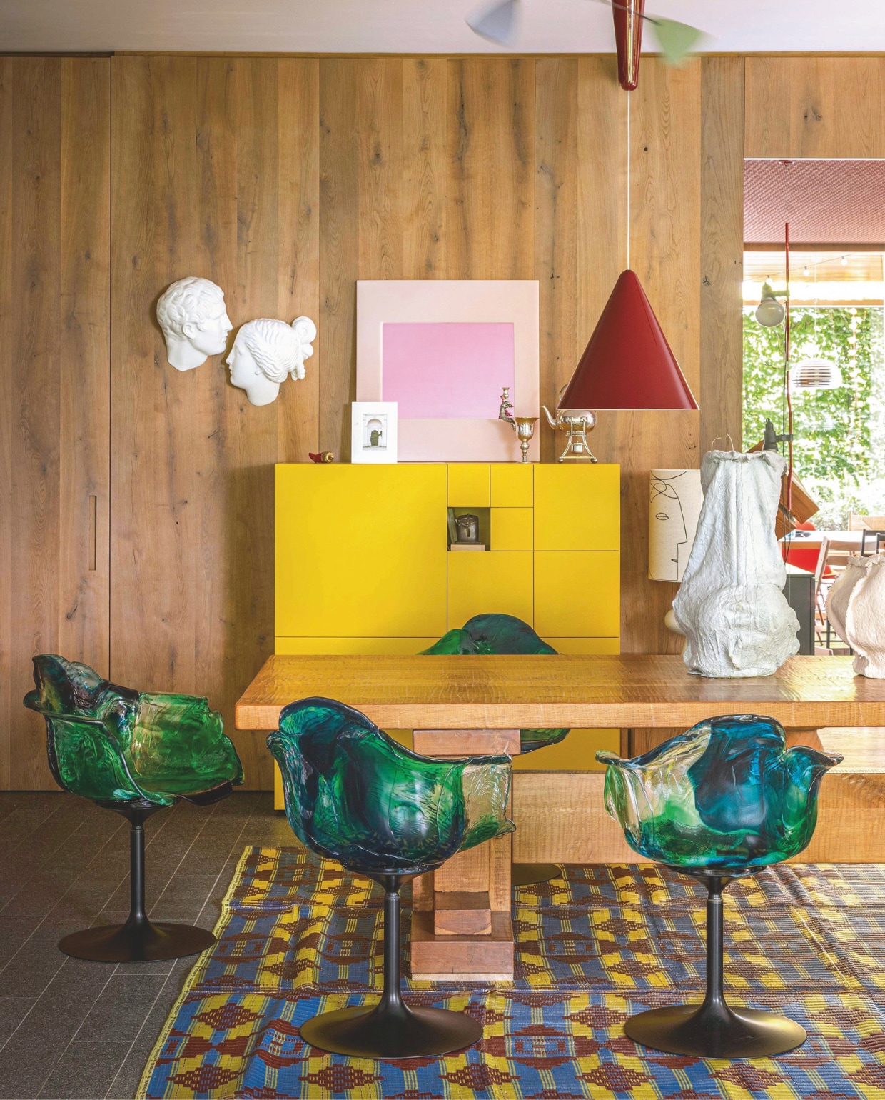 Eetkamerstoelen Ella van Edra. Rode lamp Diabolo van Flos. Tafel Rivadossi. Gele kast Conchiglia van Studiocharlie voor Lema. Porseleinen gezichten Memorabilia Mvsevm van Seletti. Afrikaans tapijt gemaakt van plastic afval. Op tafel vazen van Nacho Carbonell. vtwonen design 02-2026 | fotografie Mattia Aquila