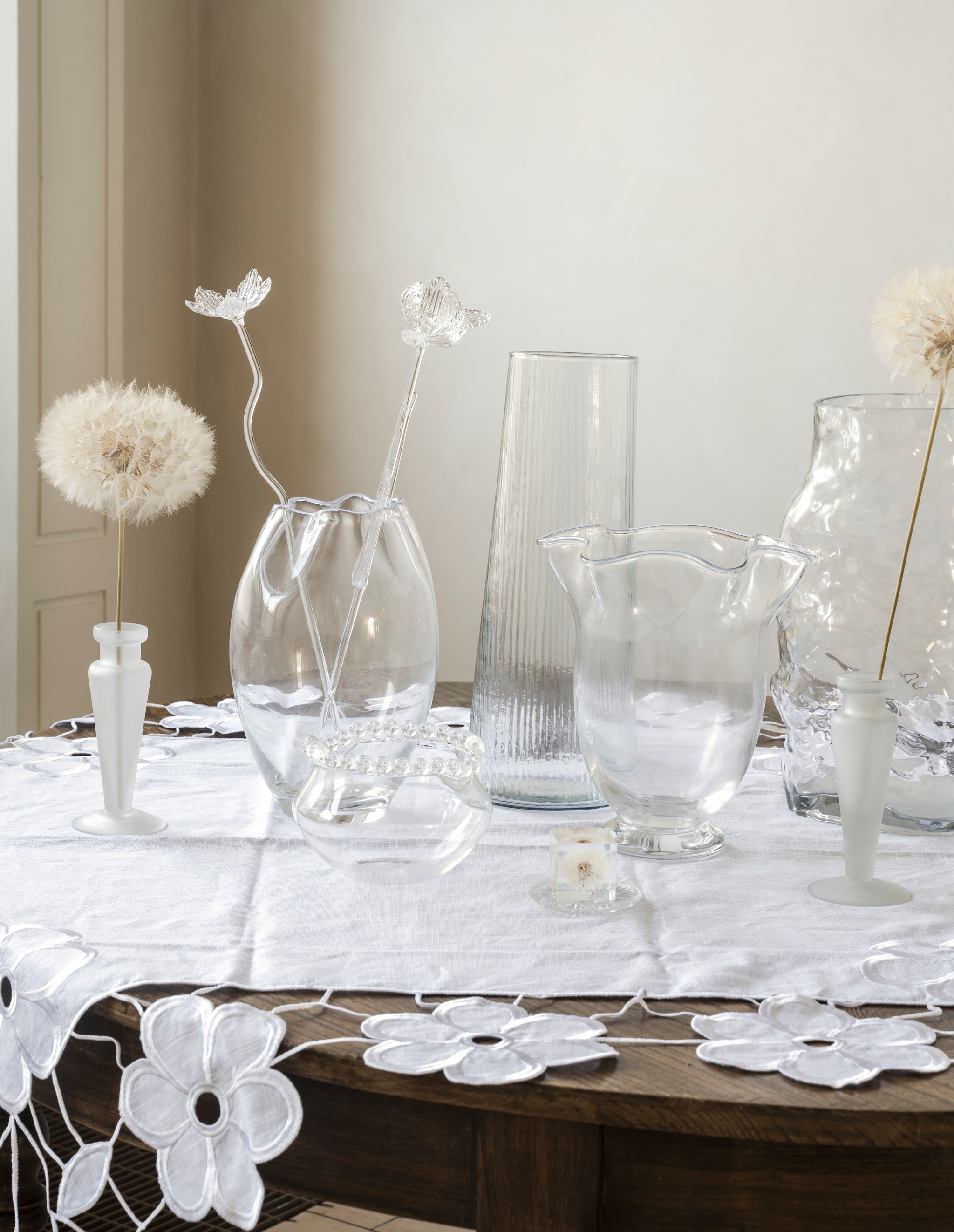 Oury Home handgemaakt tafelkleed bloemenrand, linnen, wit, 180x180 cm € 175,- (ouryhome.nl). Zara Home kandelaar Colin King (als vaas), glas € 29,99, vaas met geschulpte rand, glas € 29,99, vaas met golvende rand, glas € 39,99, gebobbelde vaas, glas € 39,99 (zarahome.com). Serax roerstaaf tulp en klaverbloem, collectie The Josephine, glas € 59,- (serax.com). Urban Nature Culture vaas Havet, gerecycled geribbeld glas € 39,99 (shop.vtwonen.nl). H&m Home vaas, gehamerd glas € 49,99 (hm.com). Droogbloemen Kwekerij geprepareerde pluizenbollen € 17,95 (droogbloemenkwekerij.nl). Presse-papier pluisbol € 46,- (etsy.com). Schaaltje, glas (kringloopwinkel). vtwonen Landelijk 06-2026 | styling Kim van Rossenberg | fotografie Stan Koolen